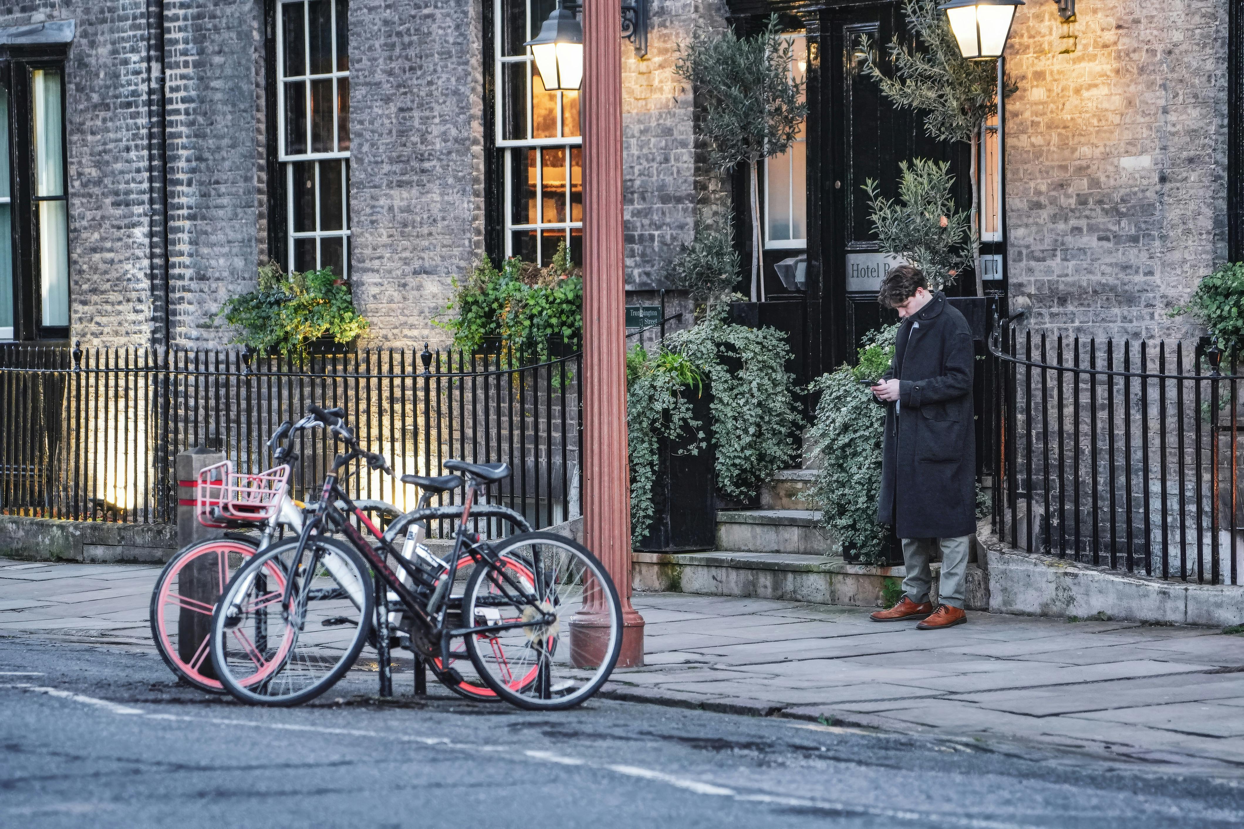 Urban street view with parked bicycles and a pedestrian outside a lit building at dusk.