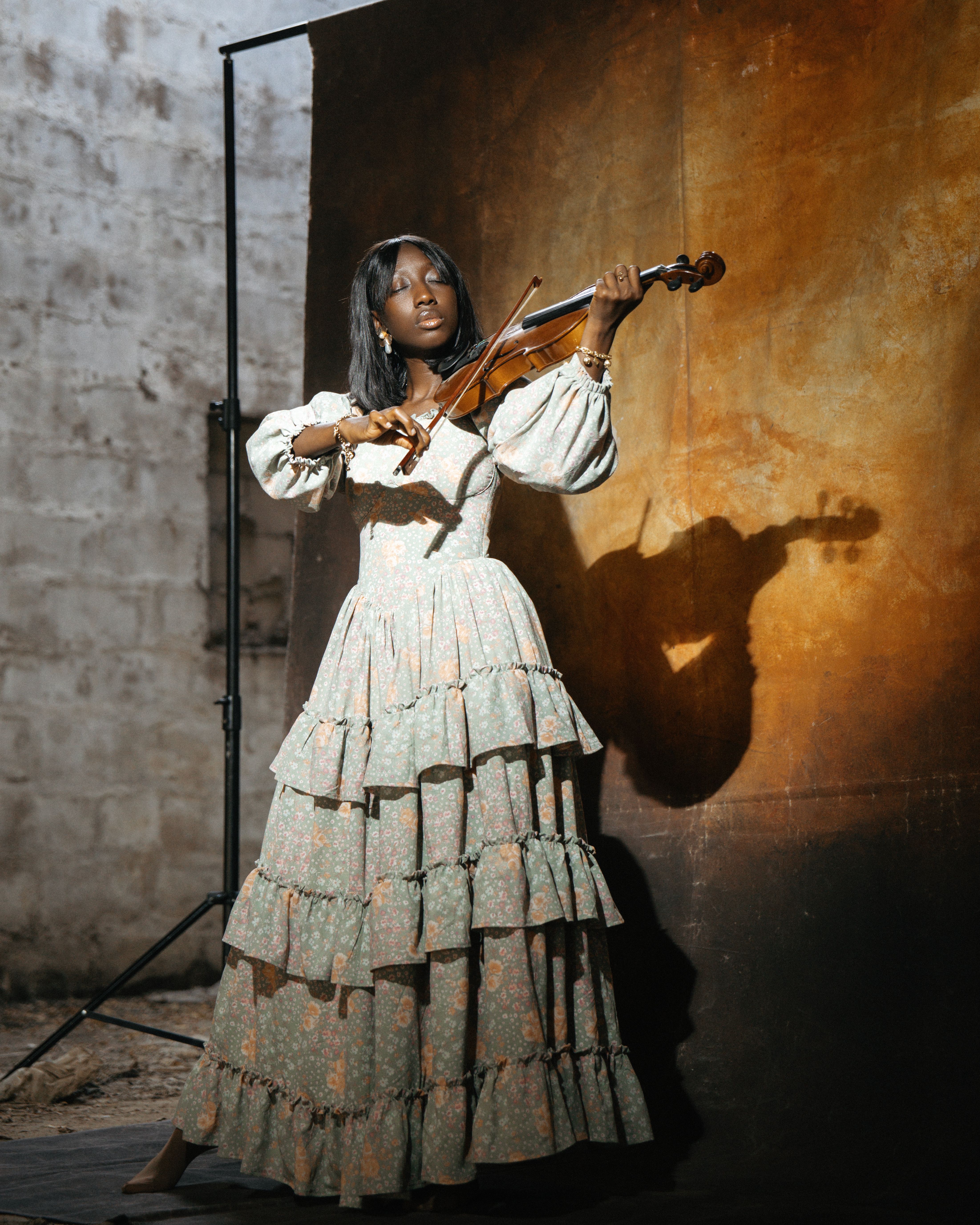 A young woman in a vintage dress plays the violin in a rustic indoor setting.