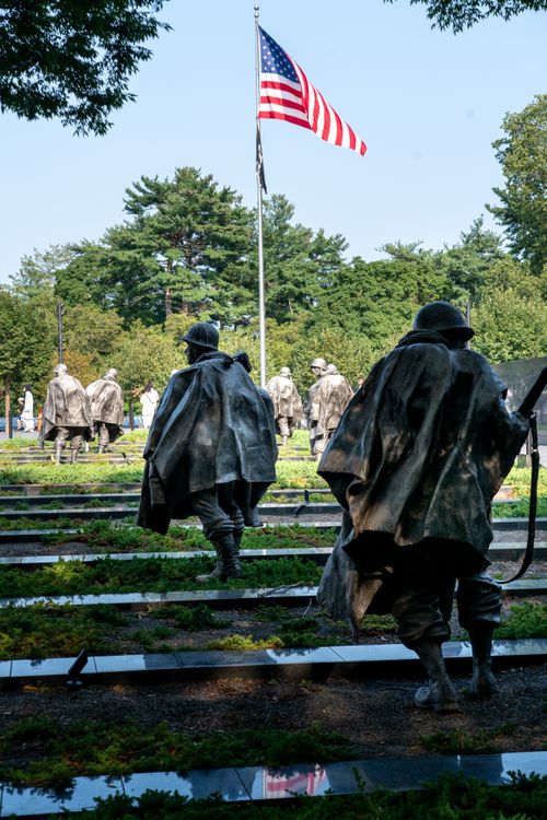Free Statues of soldiers at the Korean War Veterans Memorial in Washington D.C. with an American flag in the background. Stock Photo