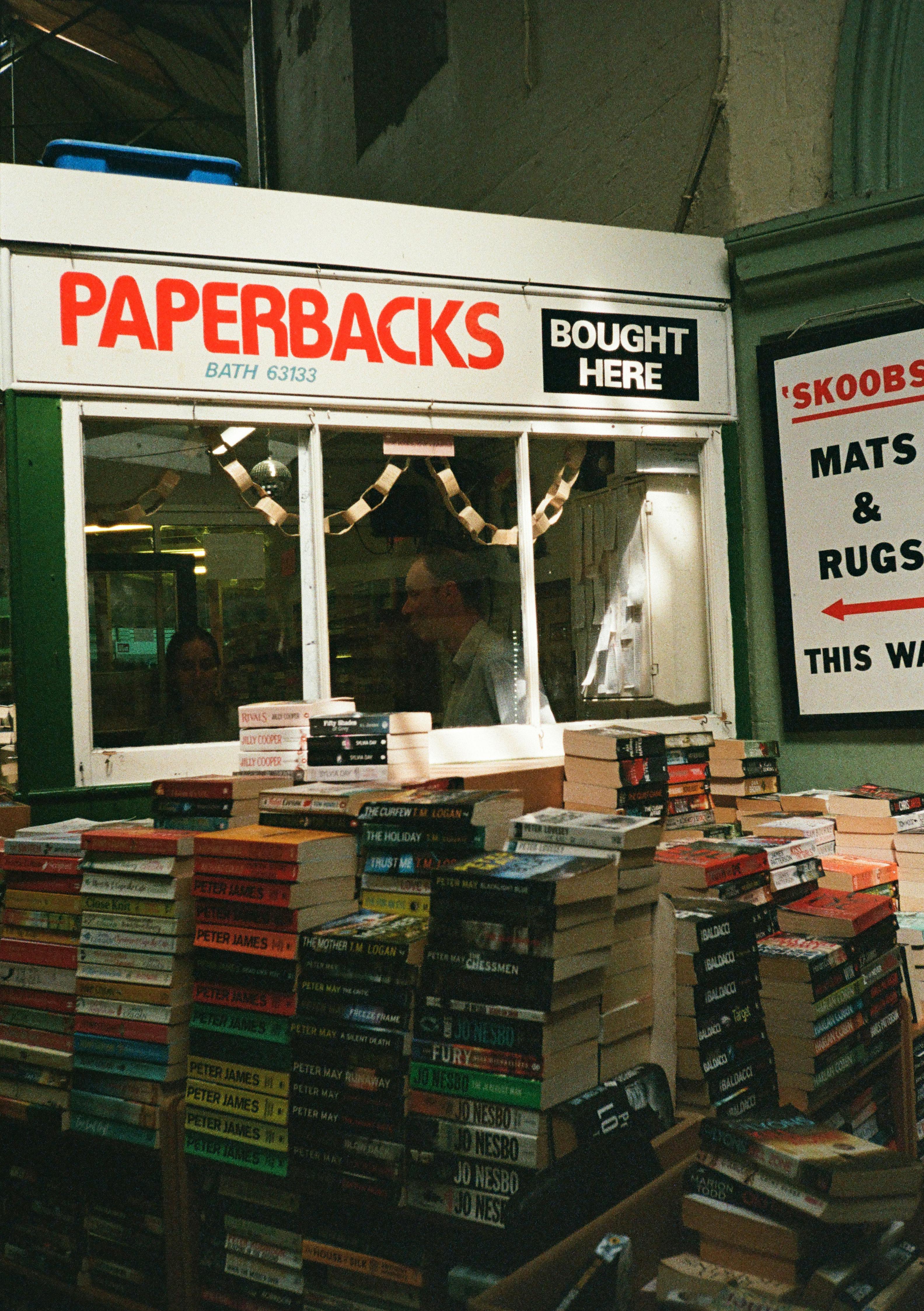 Explore a classic bookshop in Bath, England, featuring stacks of paperbacks in a cozy market setting.
