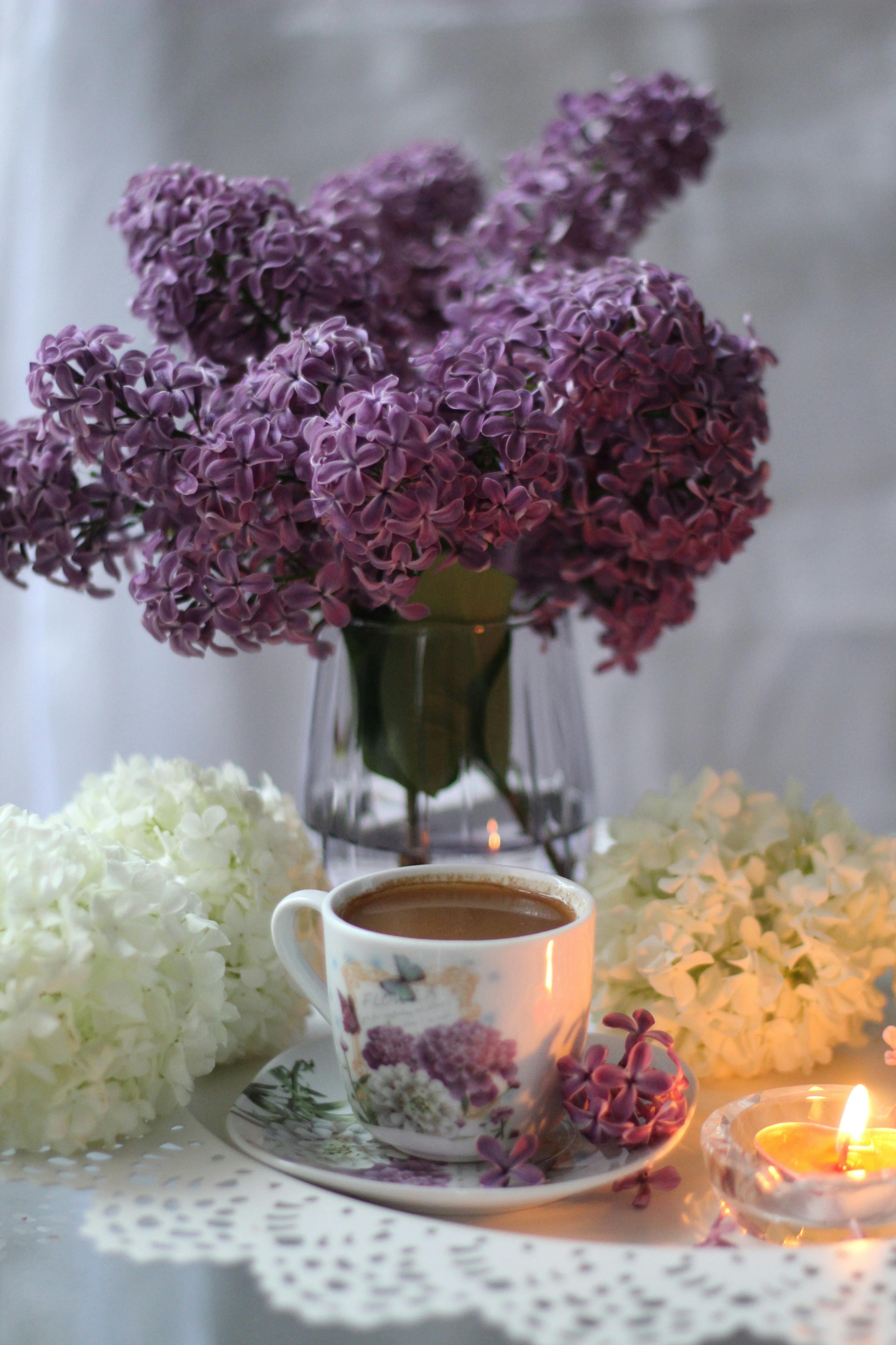 A cozy tea scene with purple lilacs, a candle, and a floral cup.