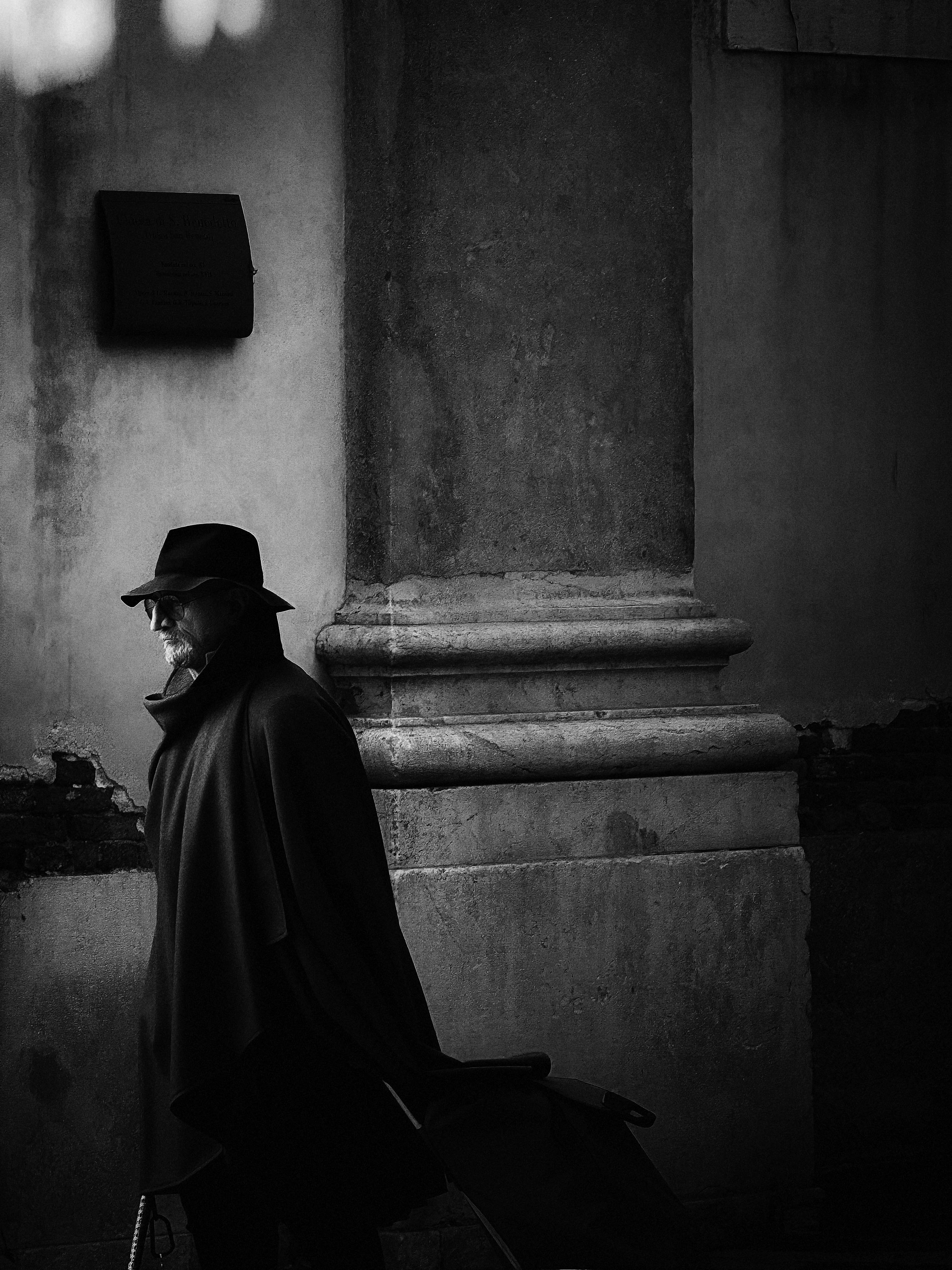 Ücretsiz İtalya'nın Venedik şehrinde, şapkalı bir adamın antik bir duvarın yanında yürürken çekilmiş siyah beyaz fotoğrafı. Stok Fotoğraflar