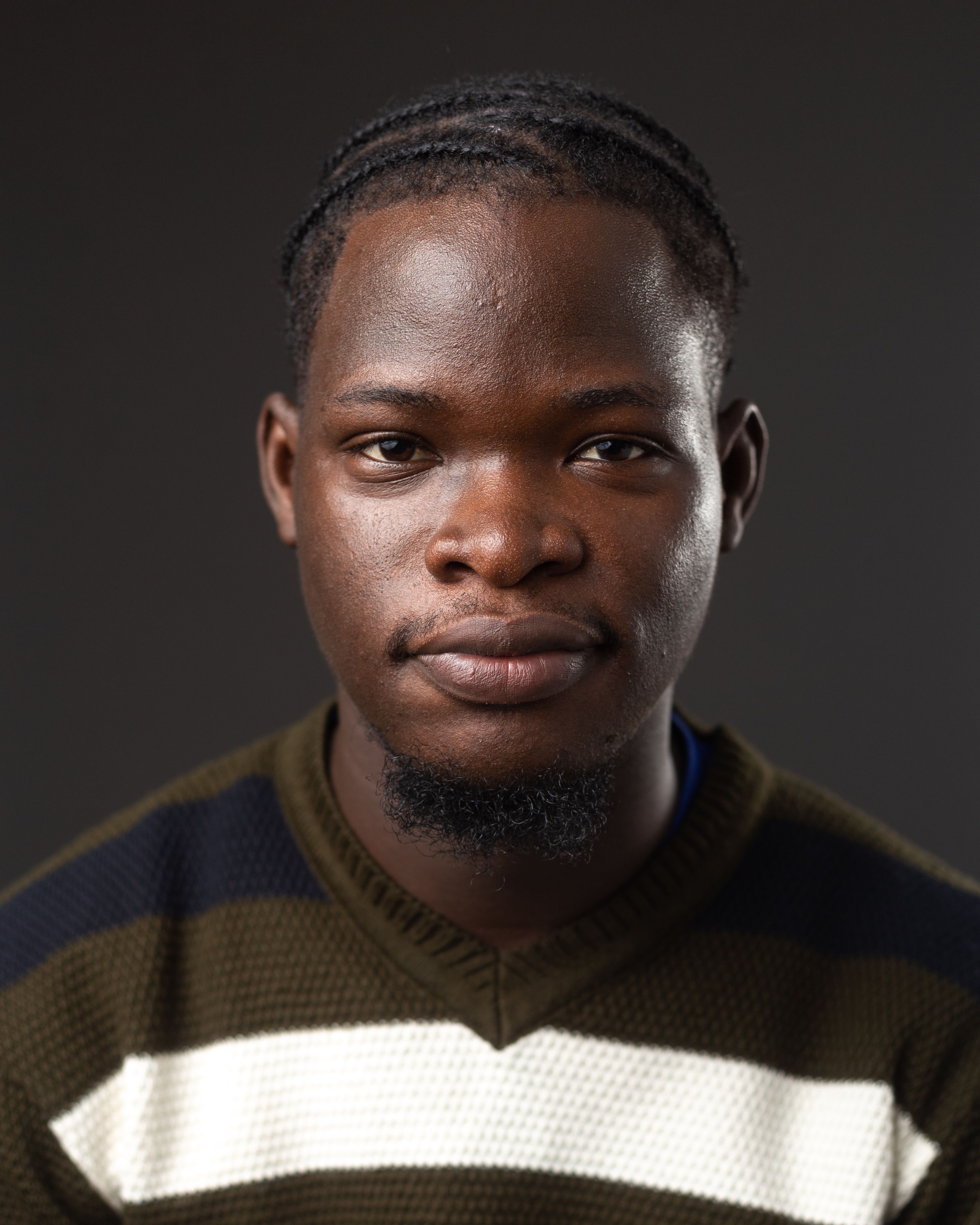 Close-up portrait of a young man wearing a striped sweater against a dark background.