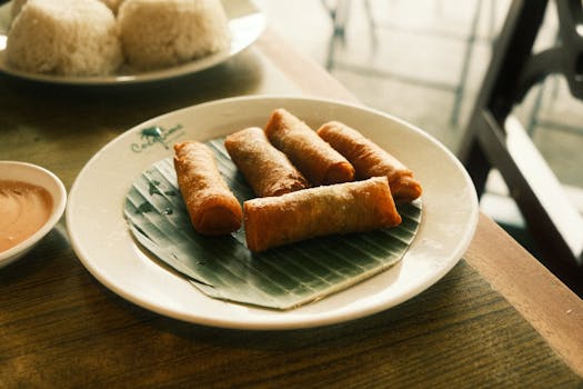 Delicious crispy spring rolls served on a banana leaf with dipping sauce, perfect for a tasty snack or appetizer.