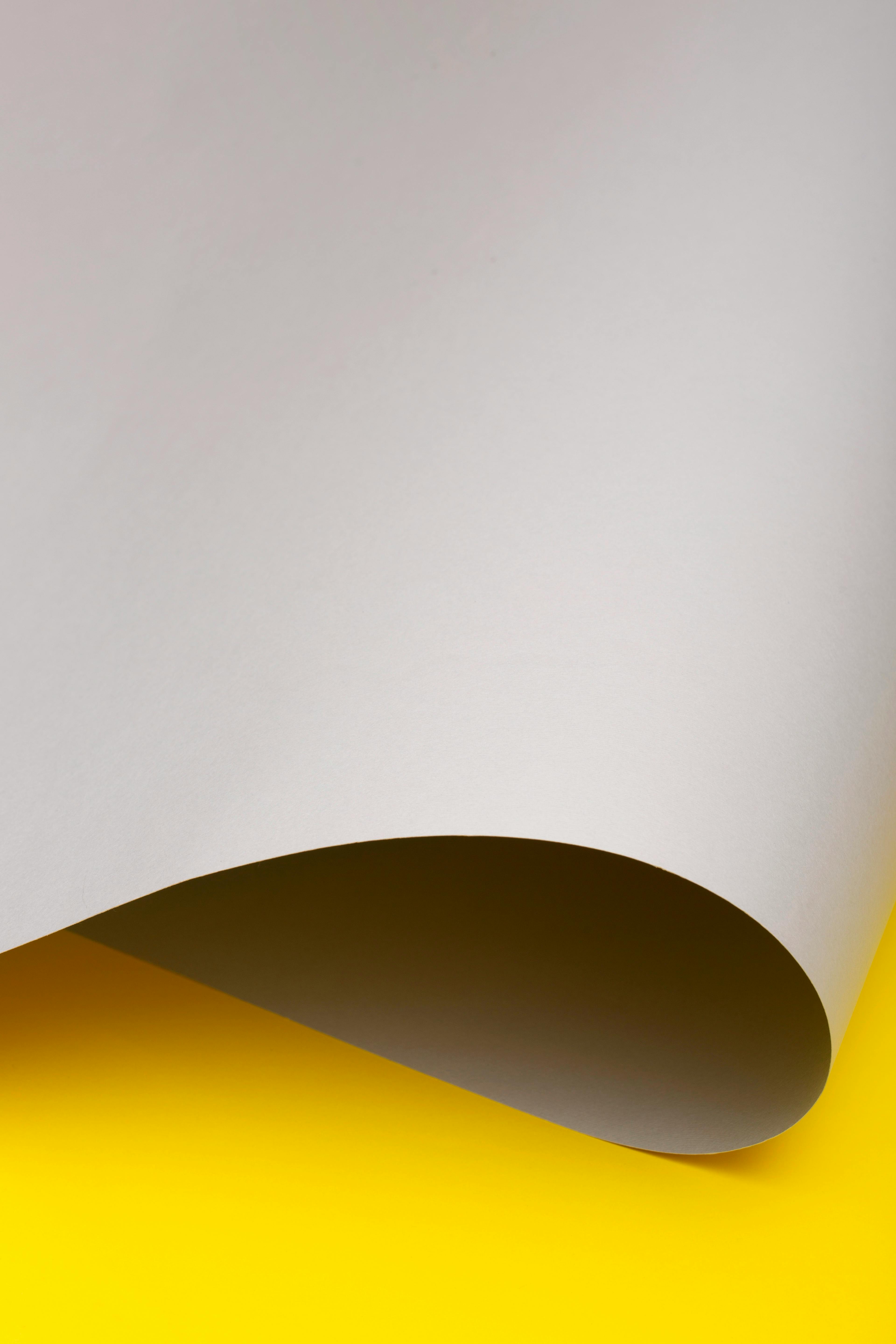 Gratis Foto minimalista di un foglio di carta bianca piegato su uno sfondo giallo brillante. Foto a disposizione