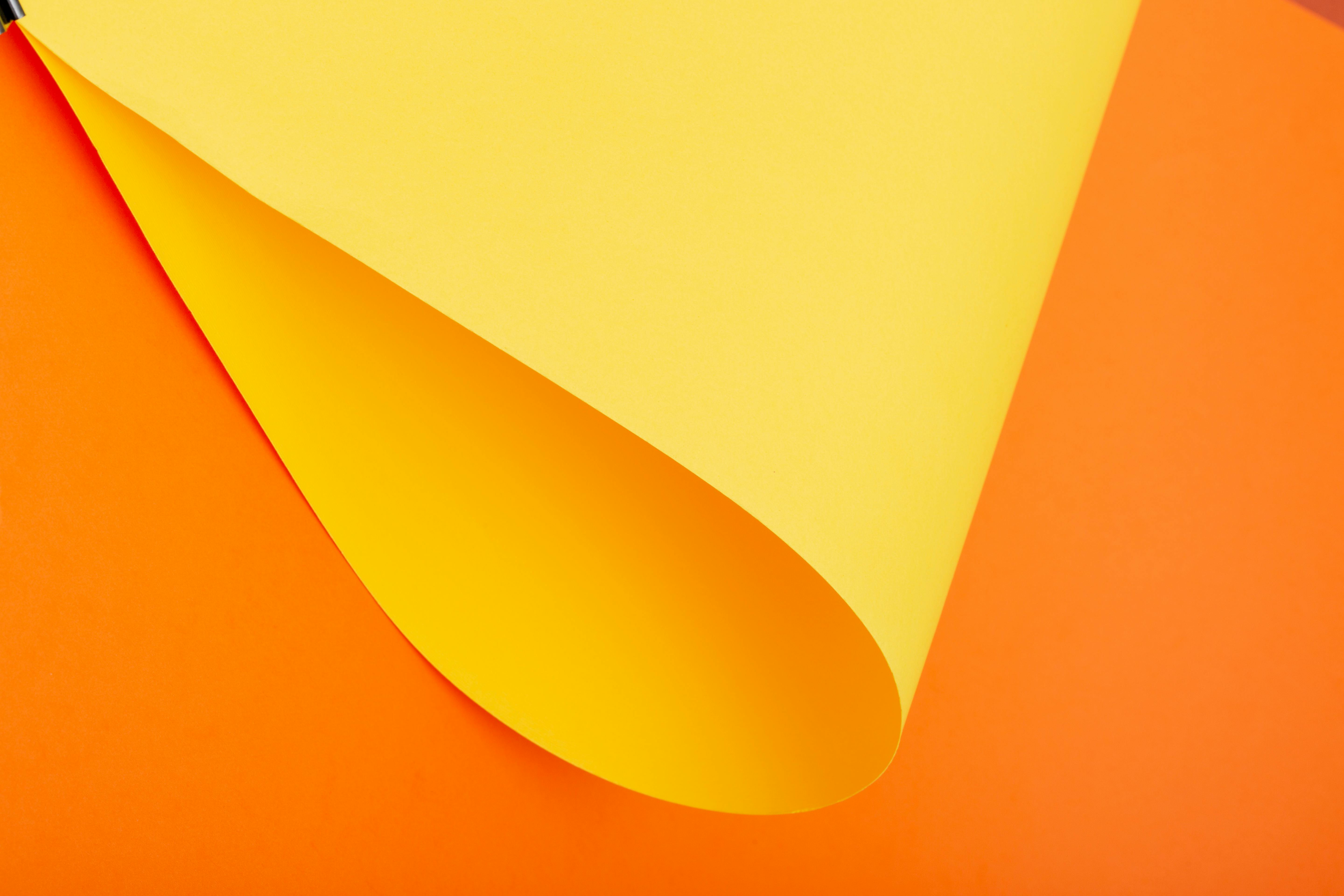 Kostenlos Leuchtend gelbes Papier, das sich über einem kräftig orangefarbenen Hintergrund wellt – ideal für kreative Designprojekte. Stock-Foto