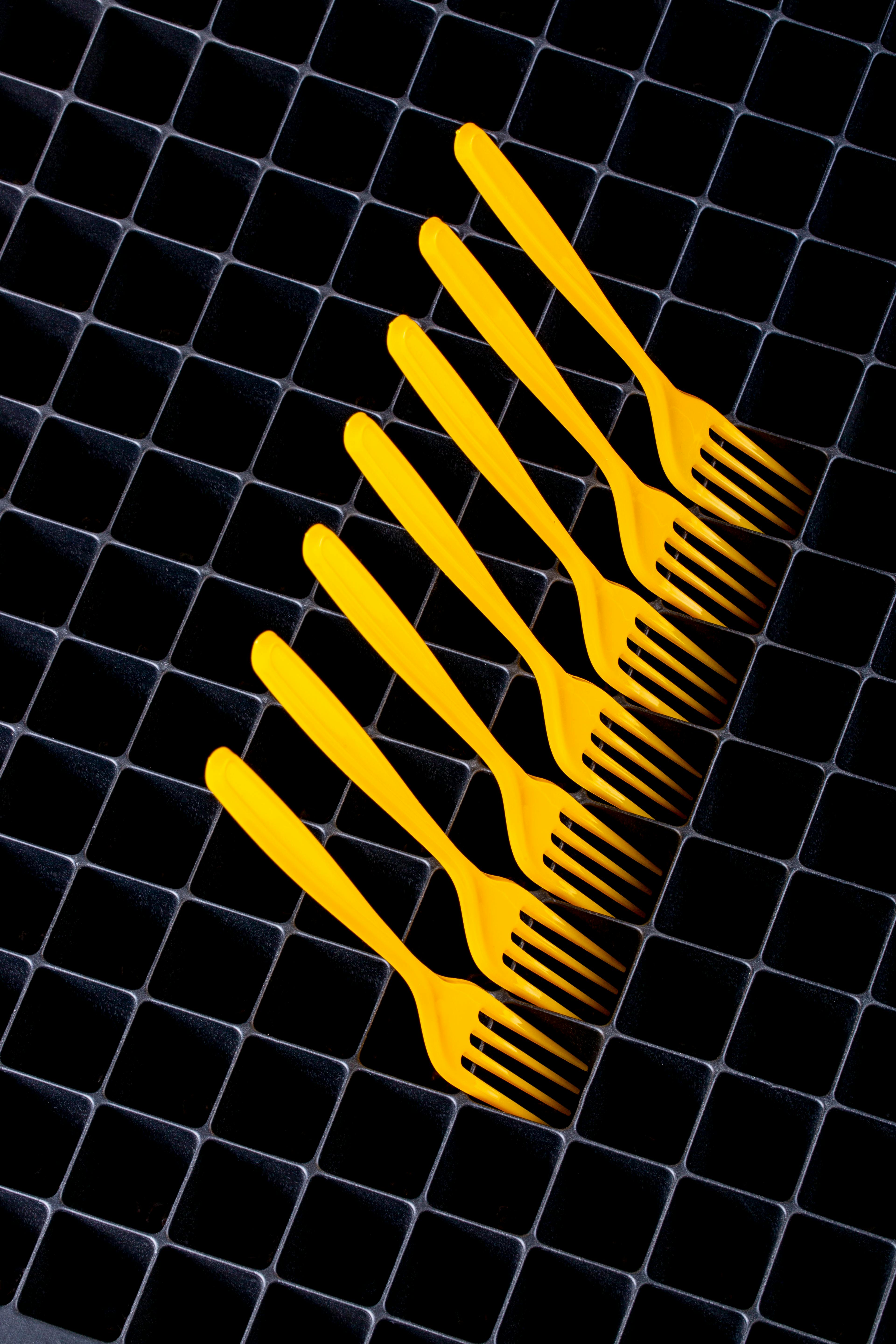 Kostenlos Minimalistische Komposition aus gelben Plastikgabeln auf schwarzem geometrischem Gittermuster. Stock-Foto