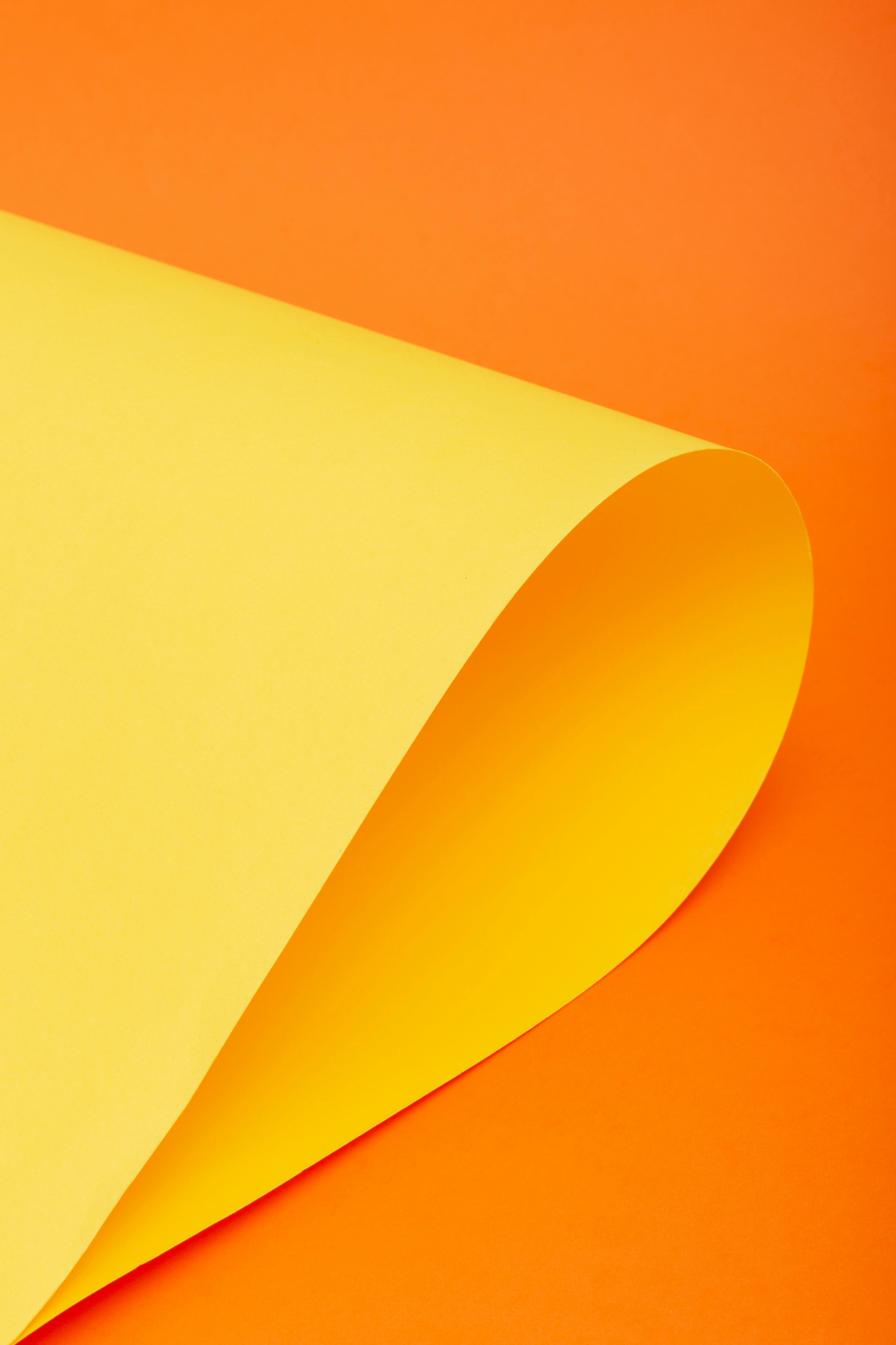 Free A vibrant yellow paper curl against a bold orange backdrop. Perfect for creative projects. Stock Photo