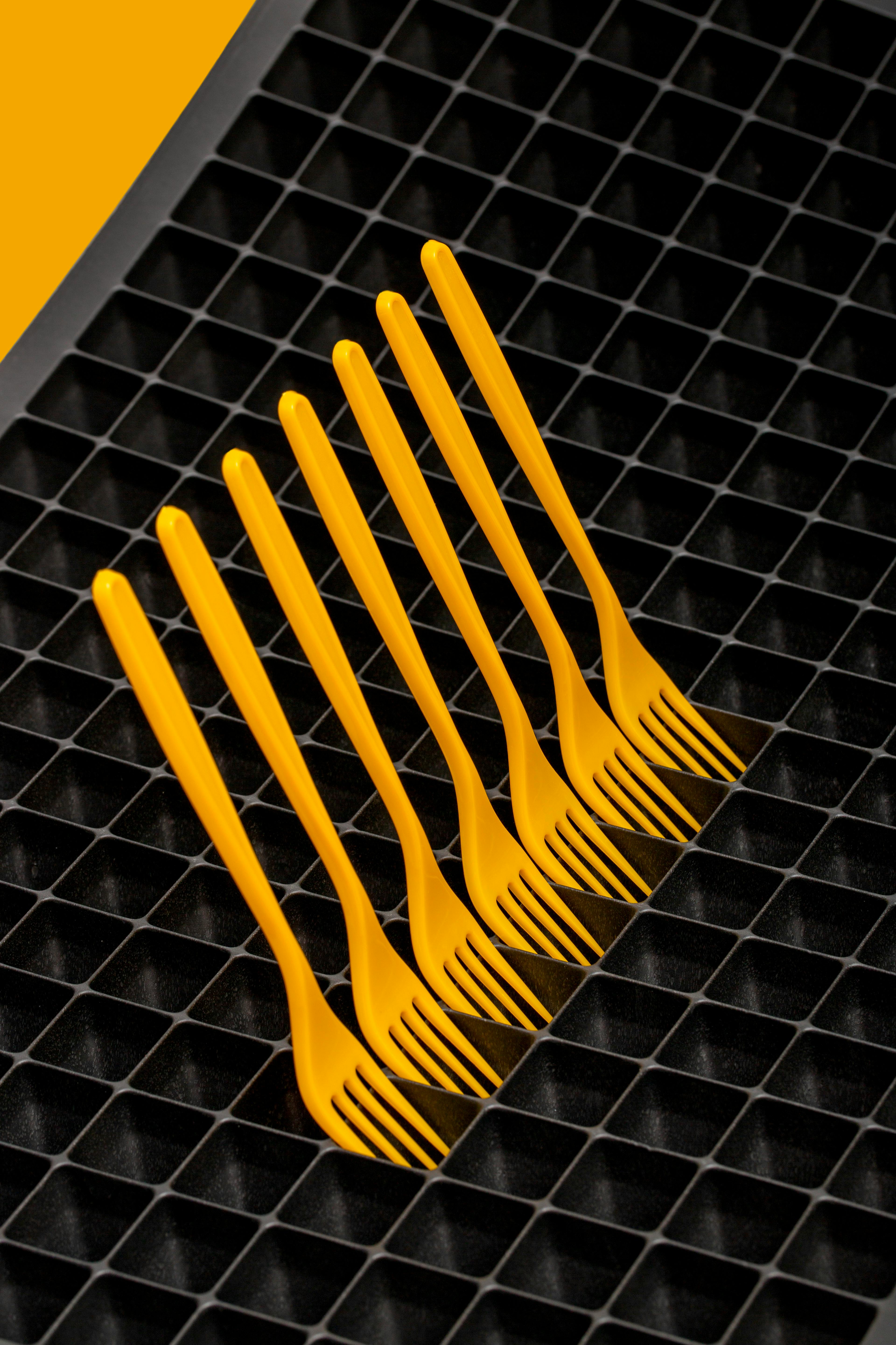 bezplatná Sedm zářivě žlutých vidliček uspořádaných na strukturovaném černém mřížkovém povrchu, které představují moderní geometrickou estetiku. Základová fotografie