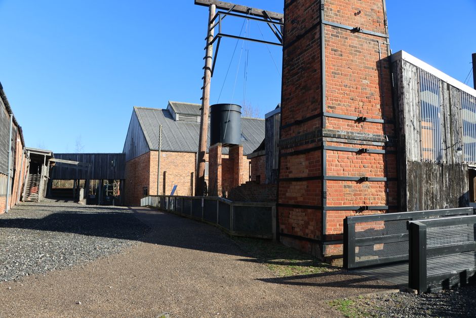 A view of historic industrial brick buildings in Marston, UK under a clear blue sky.