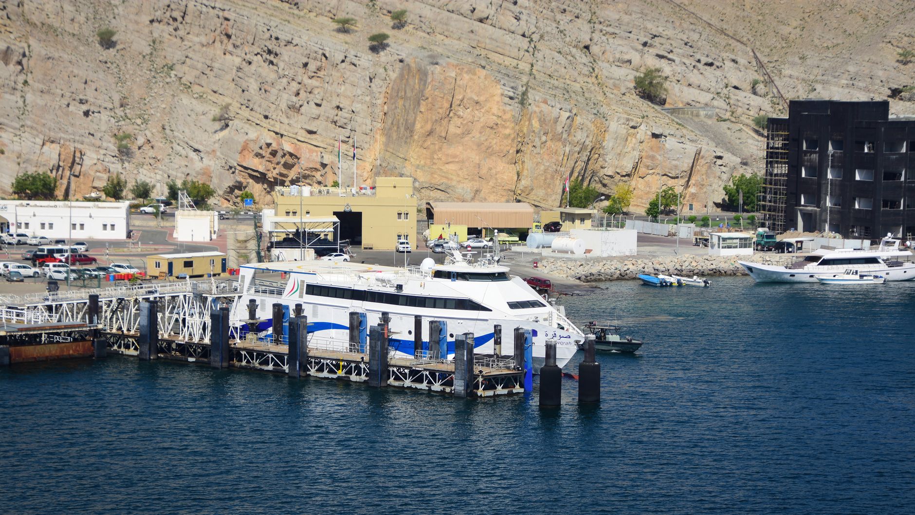 A serene view of boats docked at the Port of Al-Chasab in Musandam, Oman with mountainous backdrop.