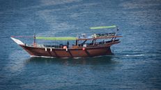 A traditional dhow boat sailing the clear waters of Musandam, Oman, under a bright day.