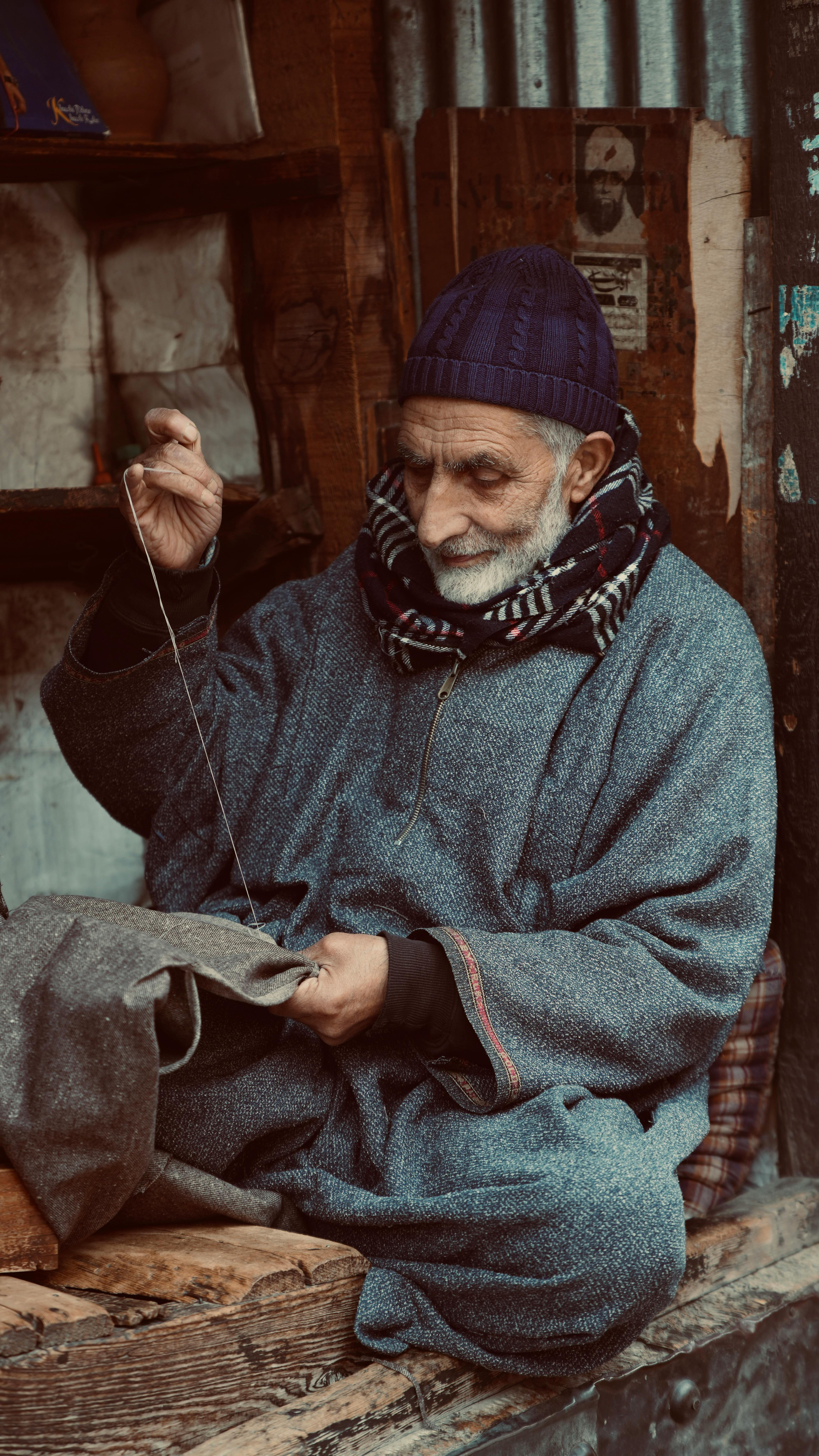 Free Elderly man sewing in traditional Kashmiri attire, Srinagar street scene. Stock Photo