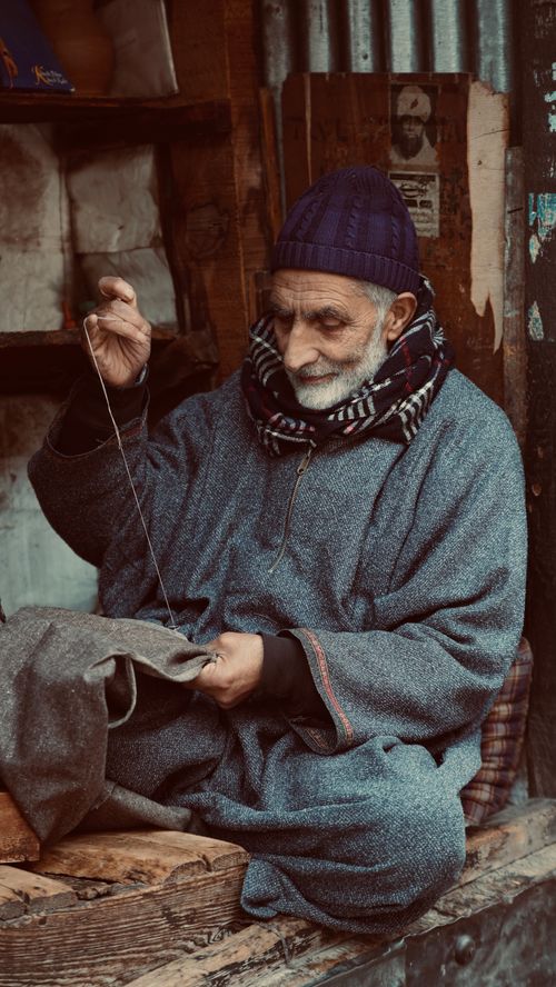 Free Elderly man sewing in traditional Kashmiri attire, Srinagar street scene. Stock Photo