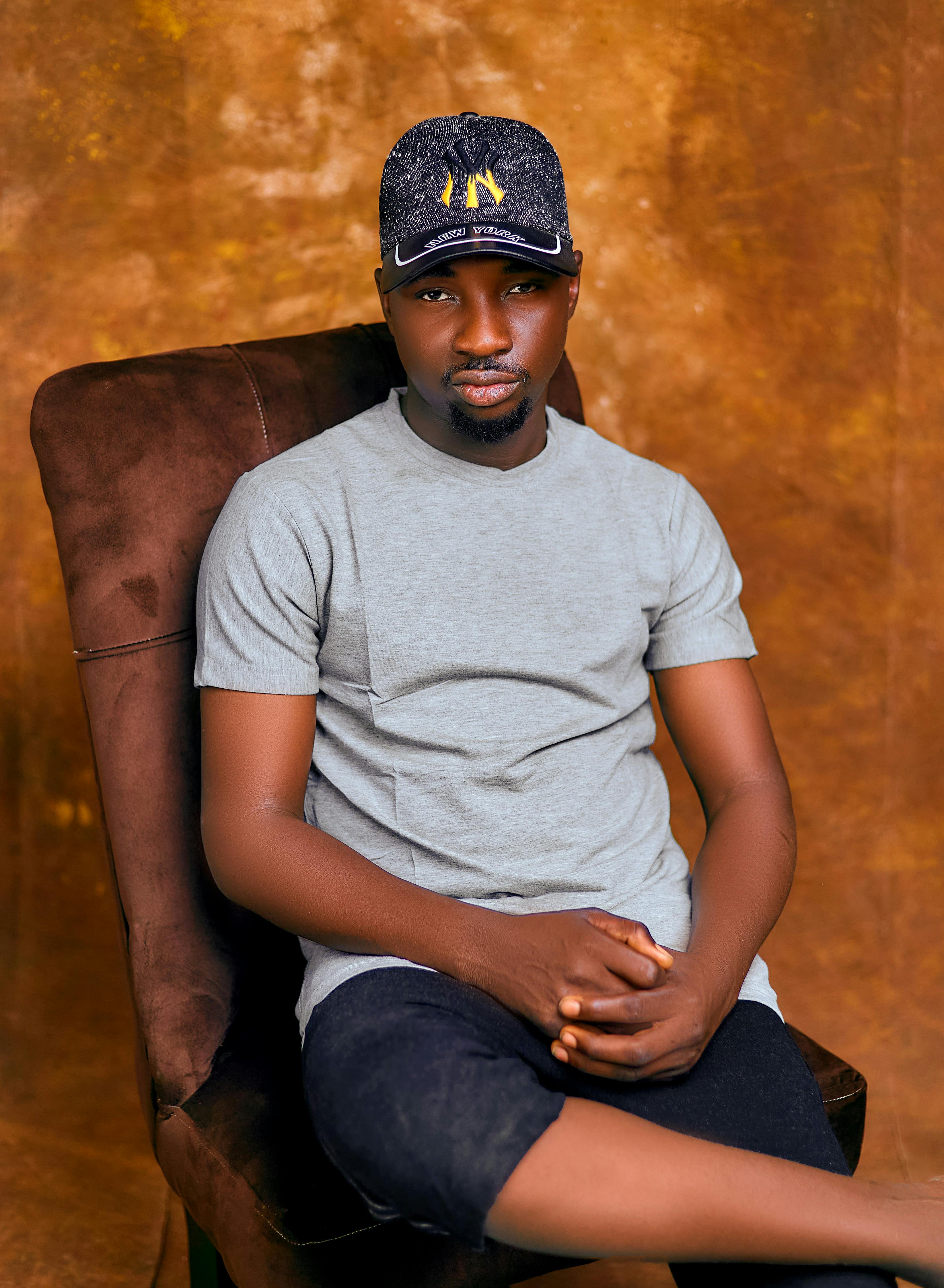 Gratis Ritratto di un uomo seduto e rilassato, con uno sfondo marrone, che indossa abiti casual e un berretto. Foto a disposizione