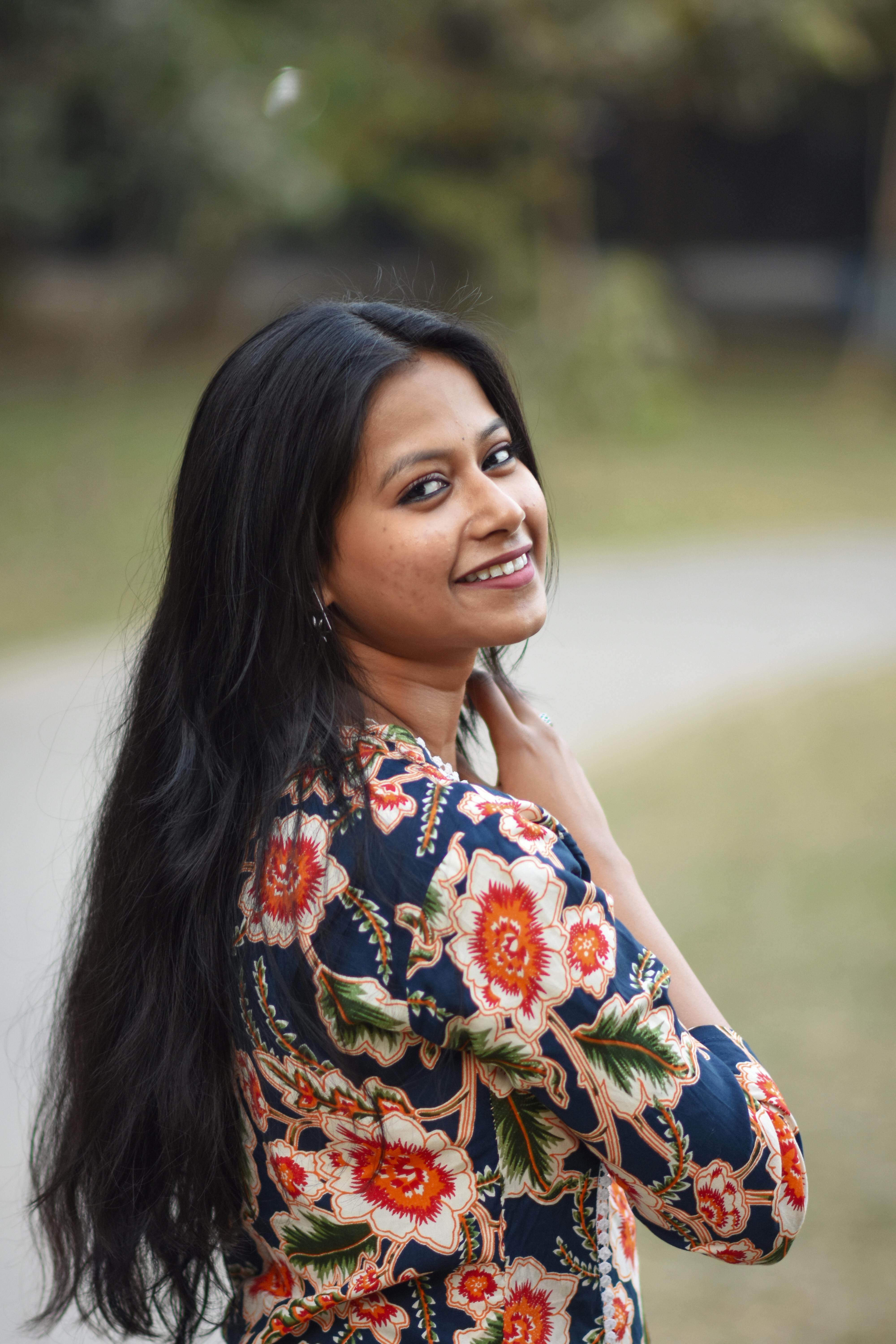 Gratis Una giovane donna con i capelli lunghi sorride indossando un abito floreale all'aperto, fotografata a Calcutta. Foto a disposizione