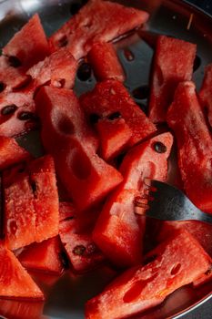 Juicy watermelon slices with seeds on a stainless steel plate and a fork.