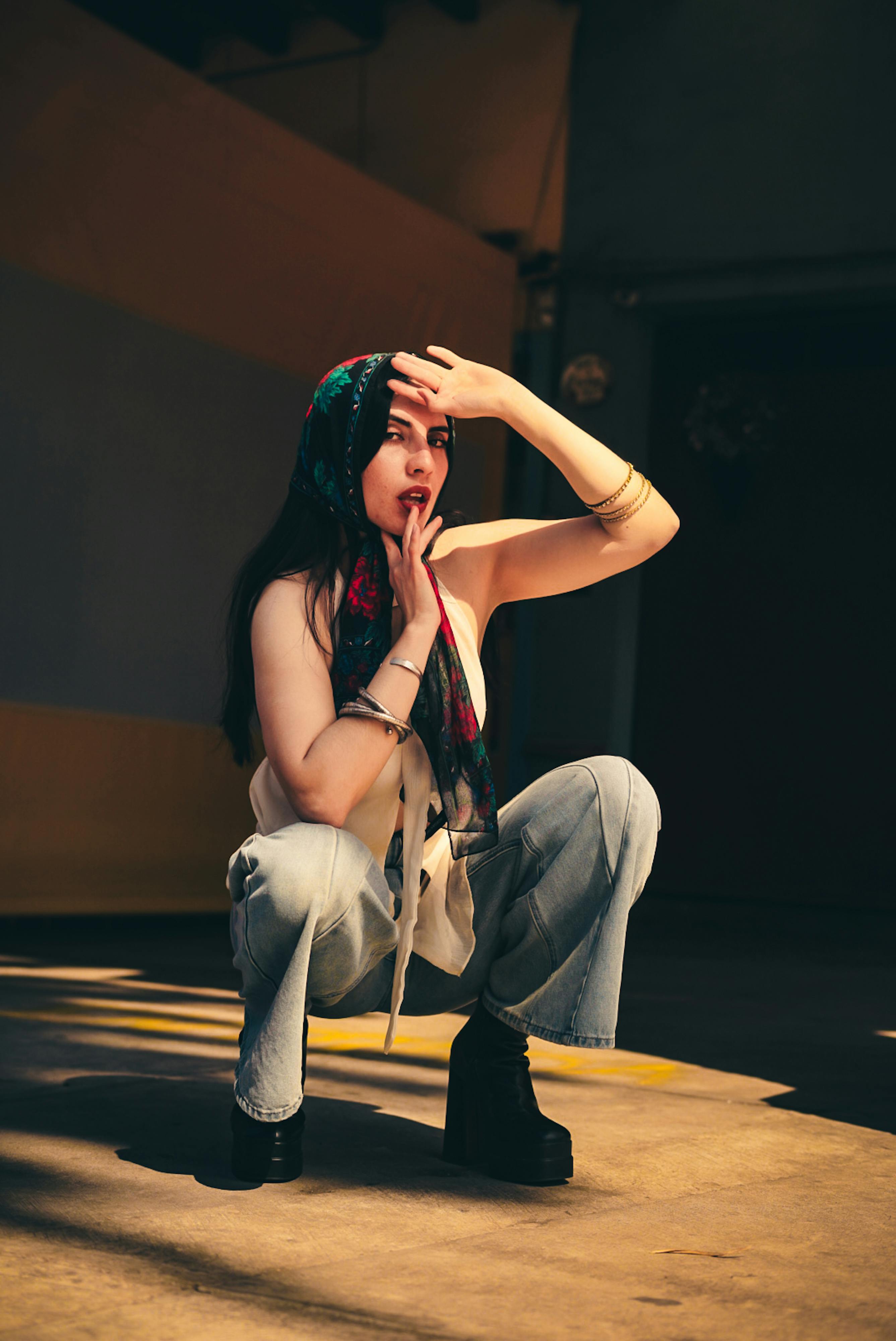 Free Young stylish woman in jeans and scarf posing dramatically in shadowy indoor setting. Stock Photo