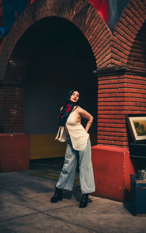 Free Stylish woman in casual attire poses confidently under a brick archway, blending modern fashion with classic architecture. Stock Photo