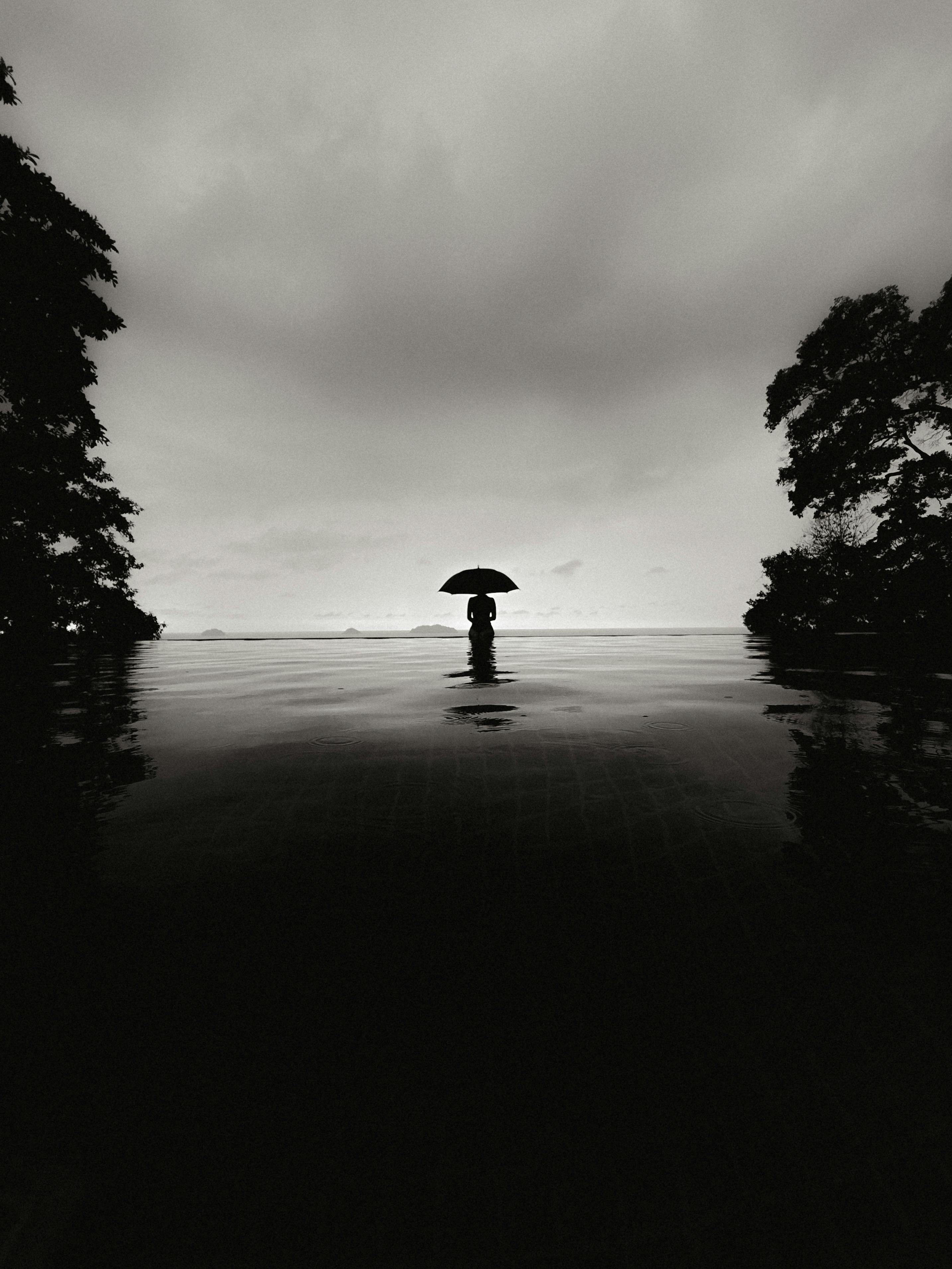 Ücretsiz Sonsuzluk havuzunda şemsiye tutan bir kişinin çarpıcı siyah beyaz silüeti, huzurlu bir atmosfer uyandırıyor. Stok Fotoğraflar