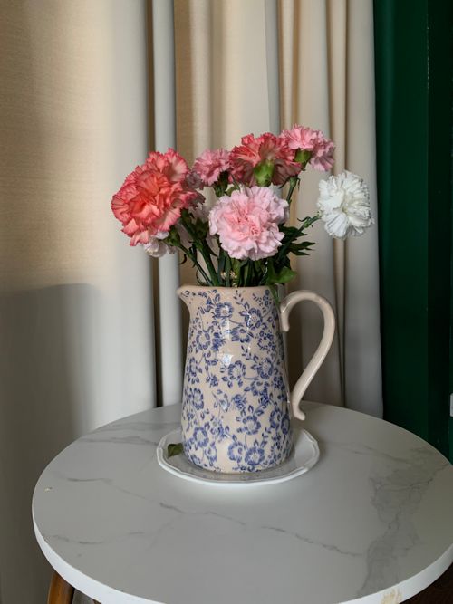 Free A charming bouquet of carnations in a blue patterned vase on a table, ideal for interior decor. Stock Photo