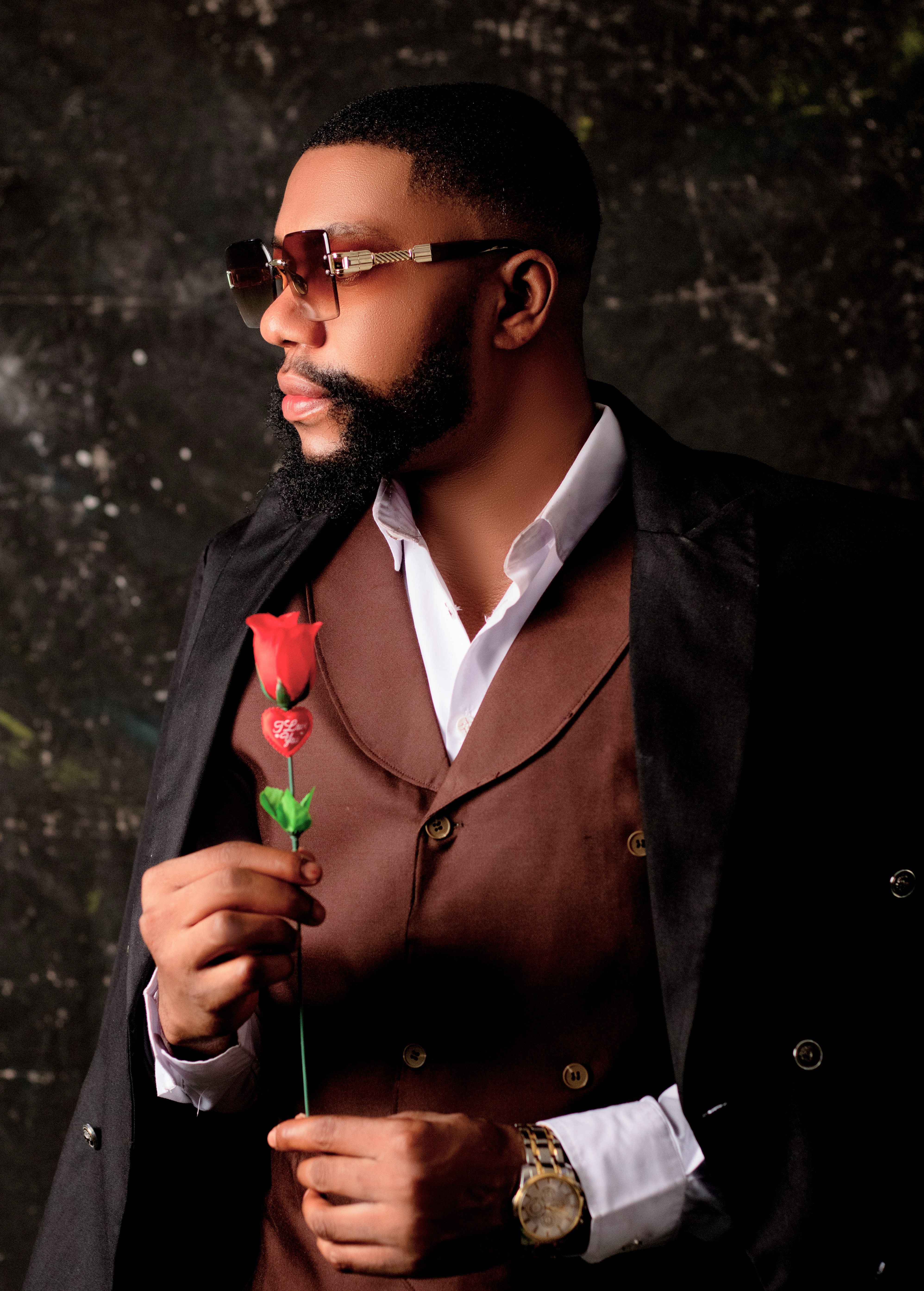 Elegant man in a suit with stylish sunglasses holding a red rose against a dark textured background.