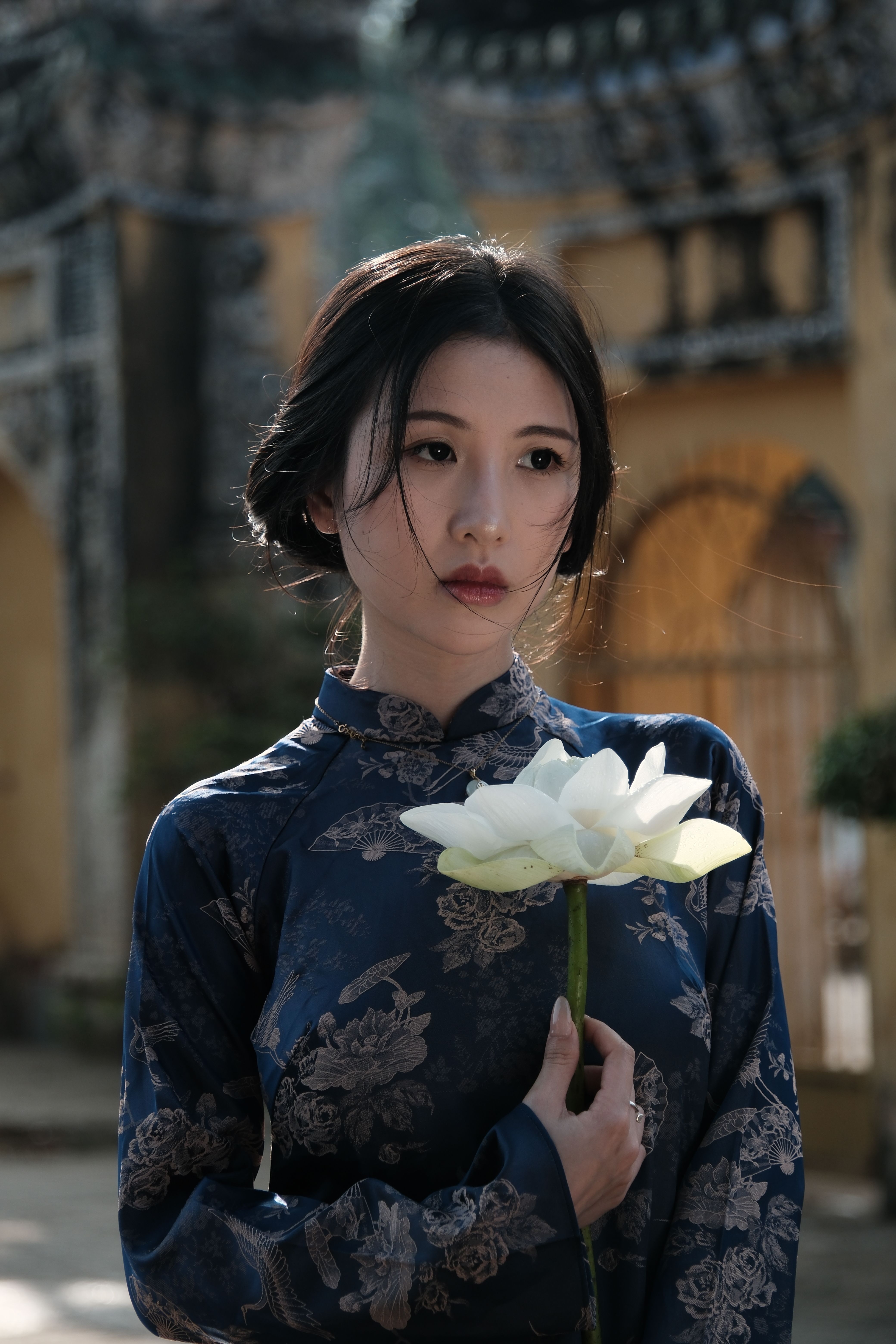 Young woman in traditional attire holding a lotus flower, conveying serenity and elegance.