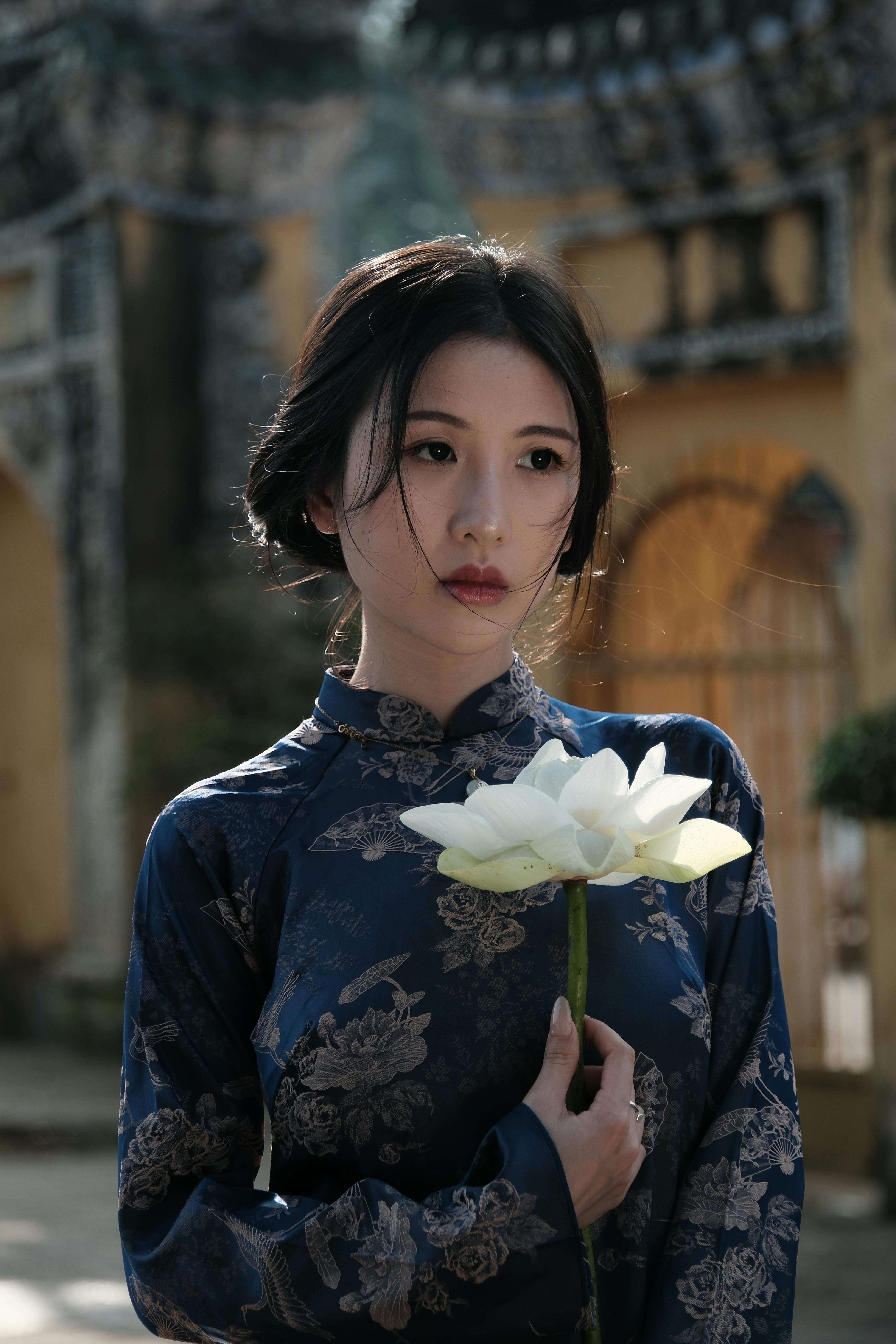 Gratis Giovane donna in abiti tradizionali che tiene in mano un fiore di loto, simbolo di serenità ed eleganza. Foto a disposizione