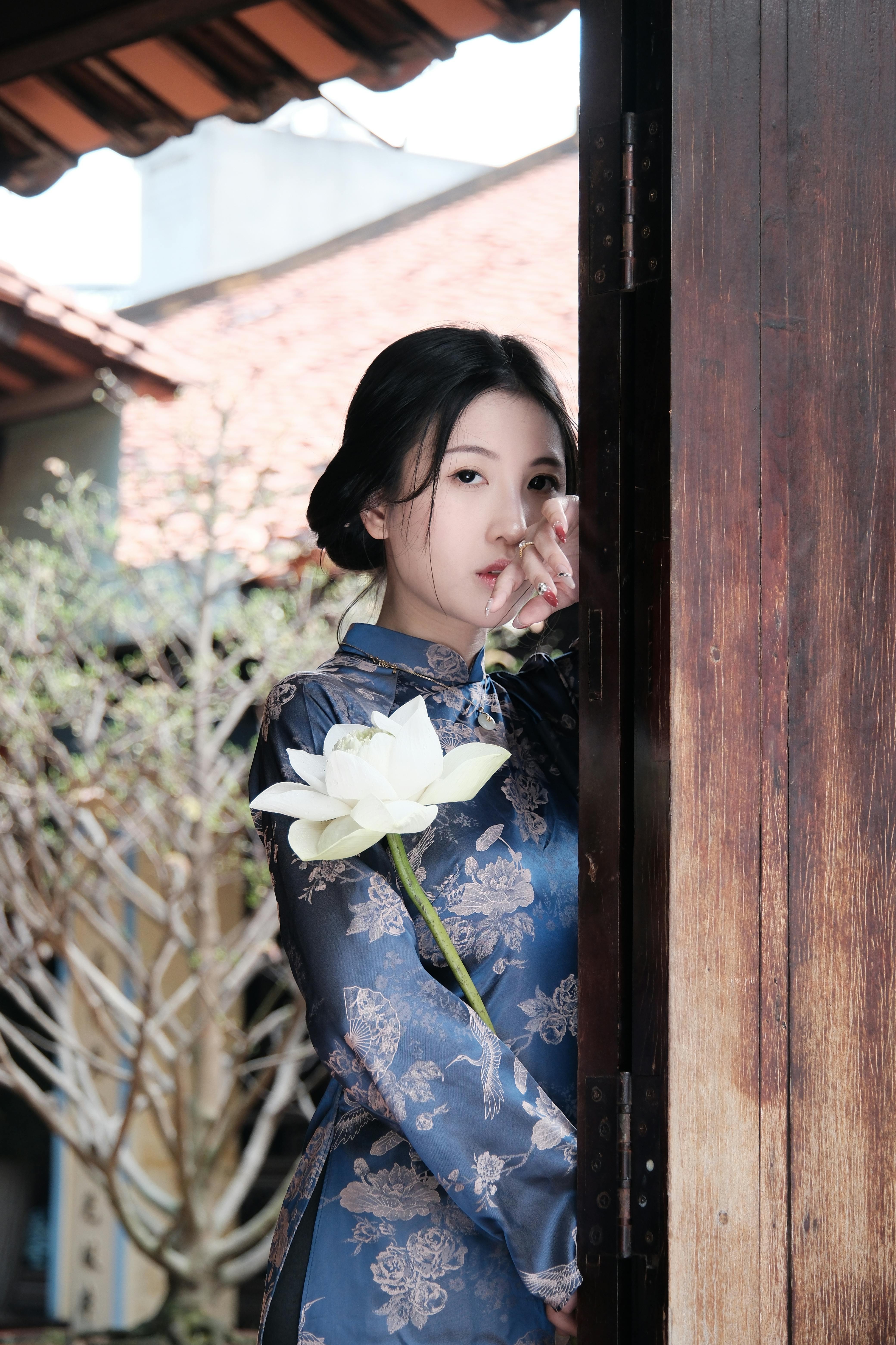 A young woman in a traditional outfit holds a lotus in a serene setting, exuding elegance and grace.
