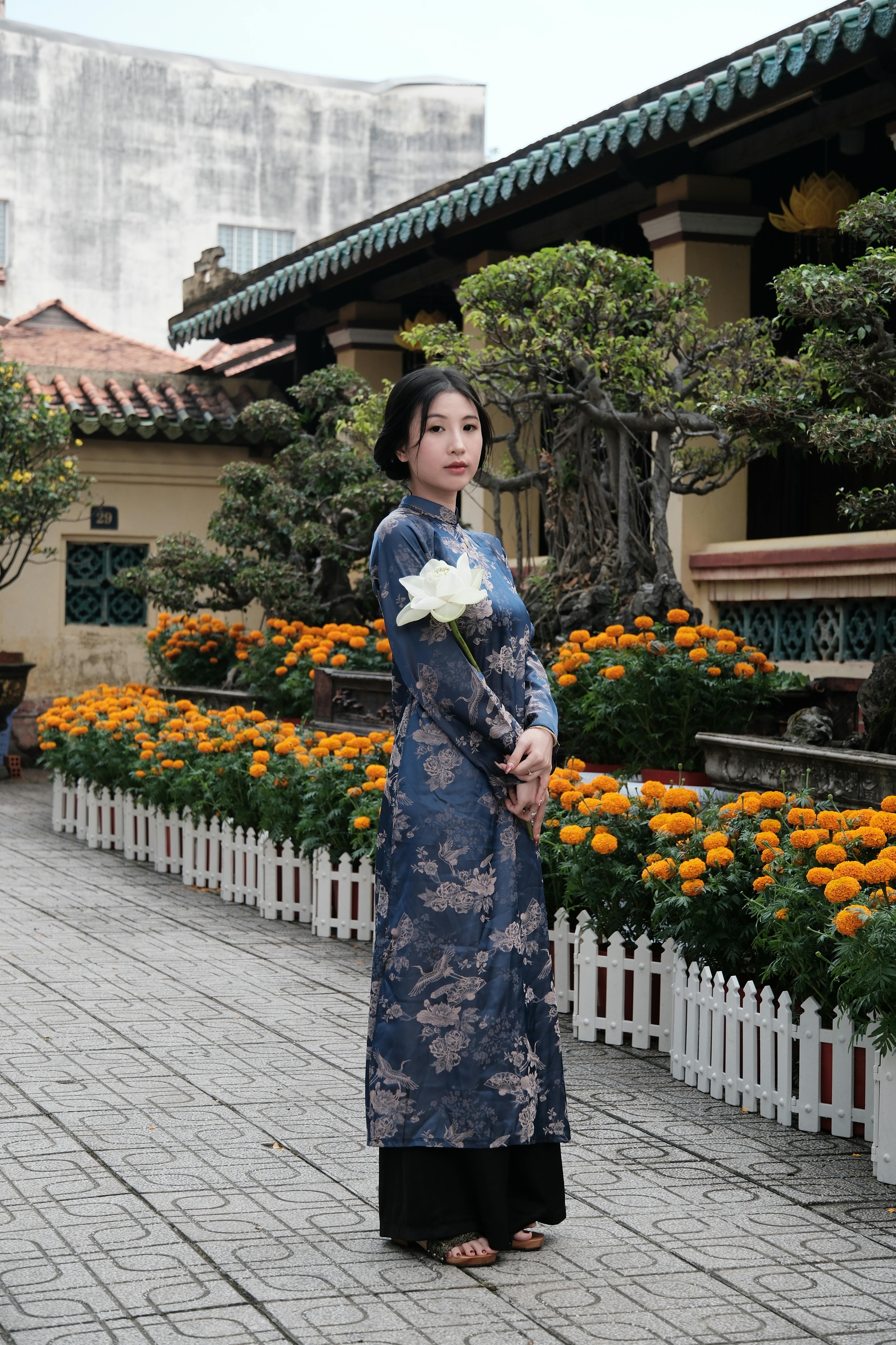 Woman in Ao Dai standing in a courtyard adorned with vibrant orange marigolds.