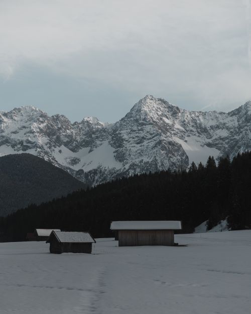 Free Serene snowy landscape in Krün, Bavaria with alpine huts and mountain backdrop. Stock Photo