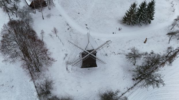 Aerial view of a historic windmill amidst a snow-blanketed rural winter scene.