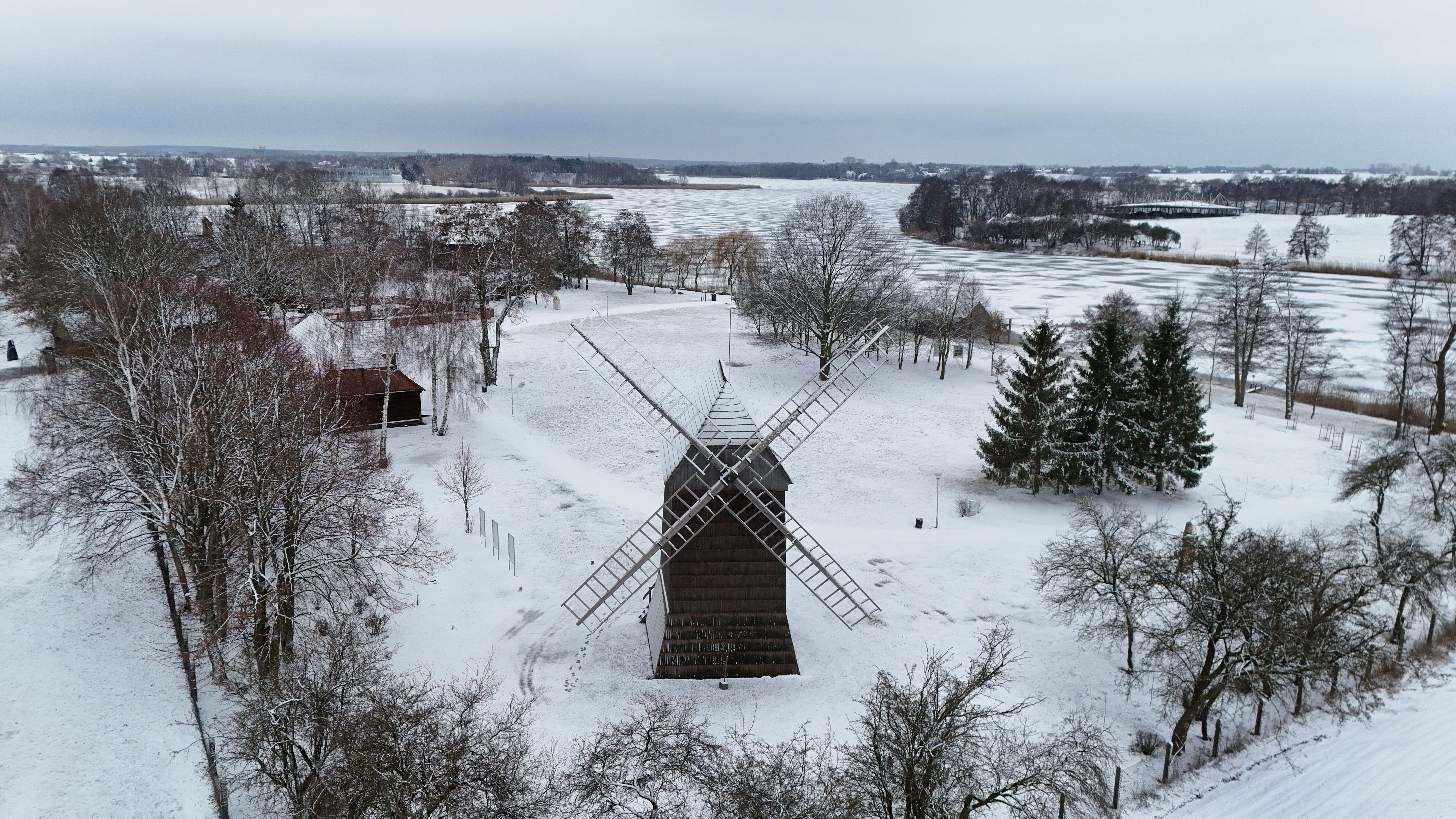 Serene winter landscape featuring a historic windmill surrounded by snow-covered trees and fields.