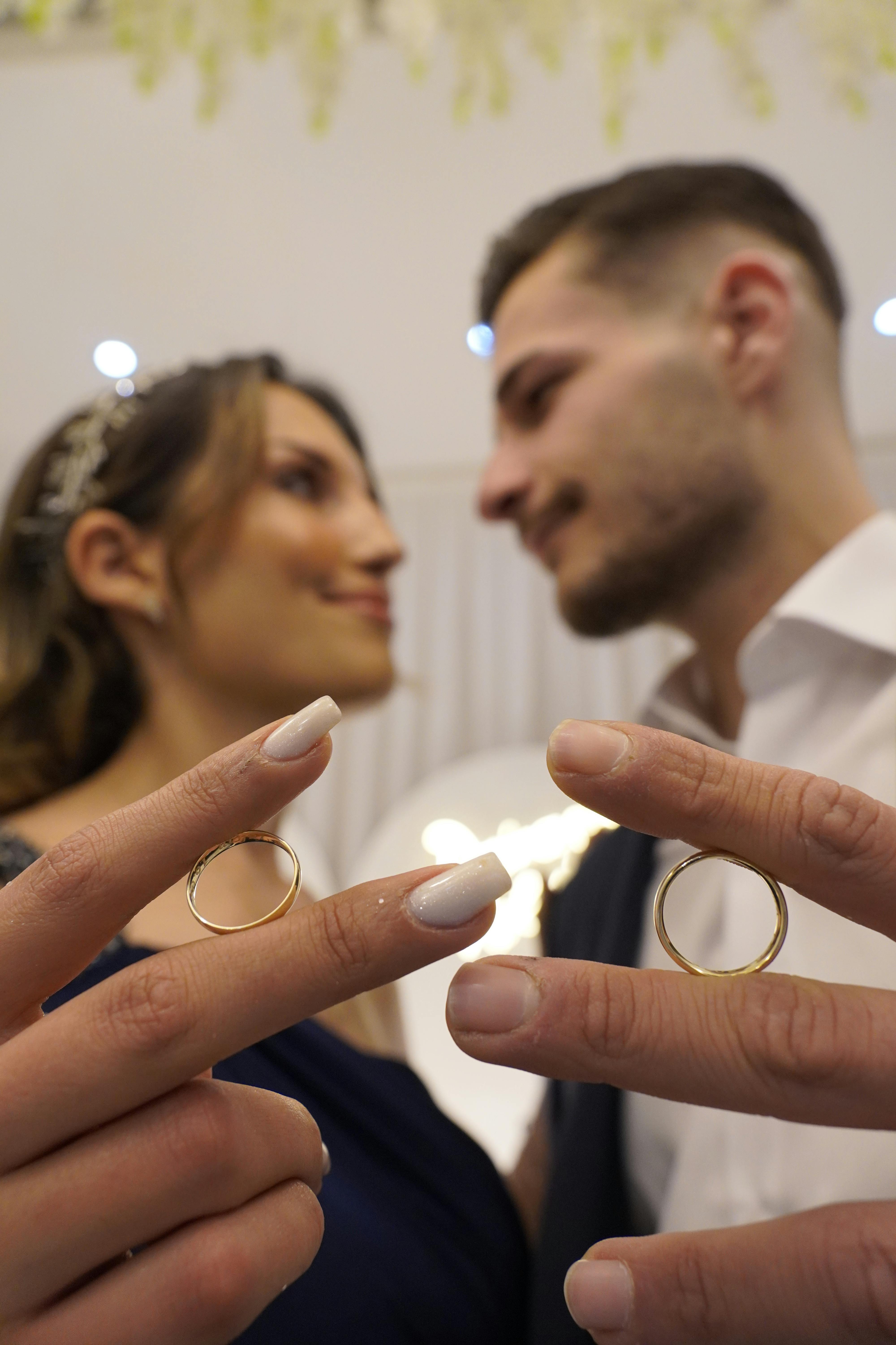 Close-up of couple holding rings, blurry background, intimate moment.