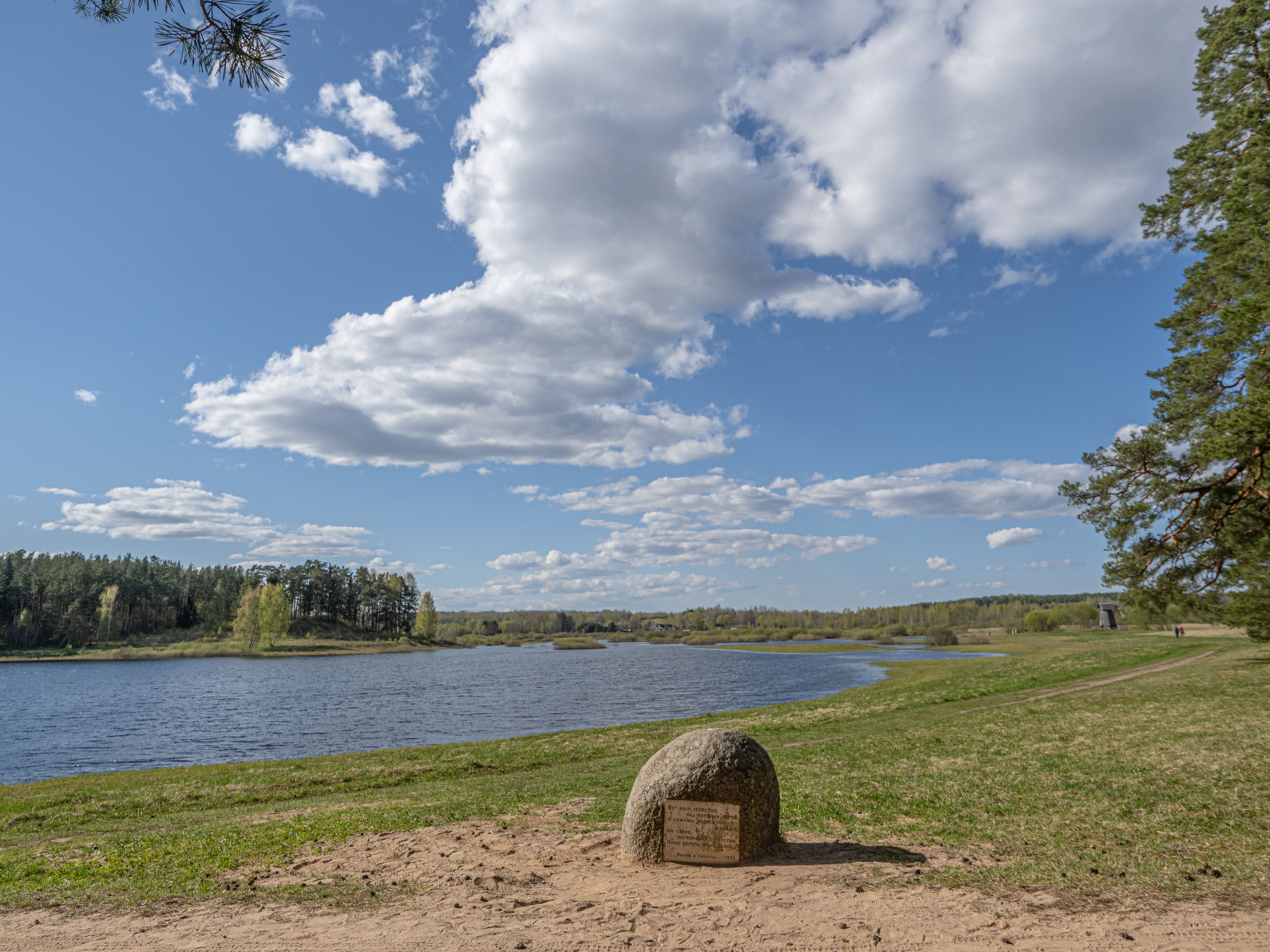 Peaceful lakeside view with lush greenery and serene clouds under a bright spring sky.