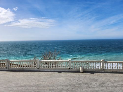 Free Beautiful view of the ocean with a stone railing and clear blue sky. Stock Photo