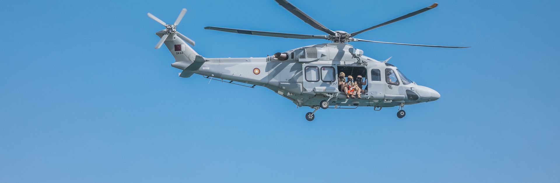 Military helicopter flying over clear blue skies in Doha, Qatar.