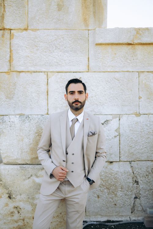 Free Stylish man in a light beige suit poses against a rustic stone wall, embodying elegance and modern fashion. Stock Photo
