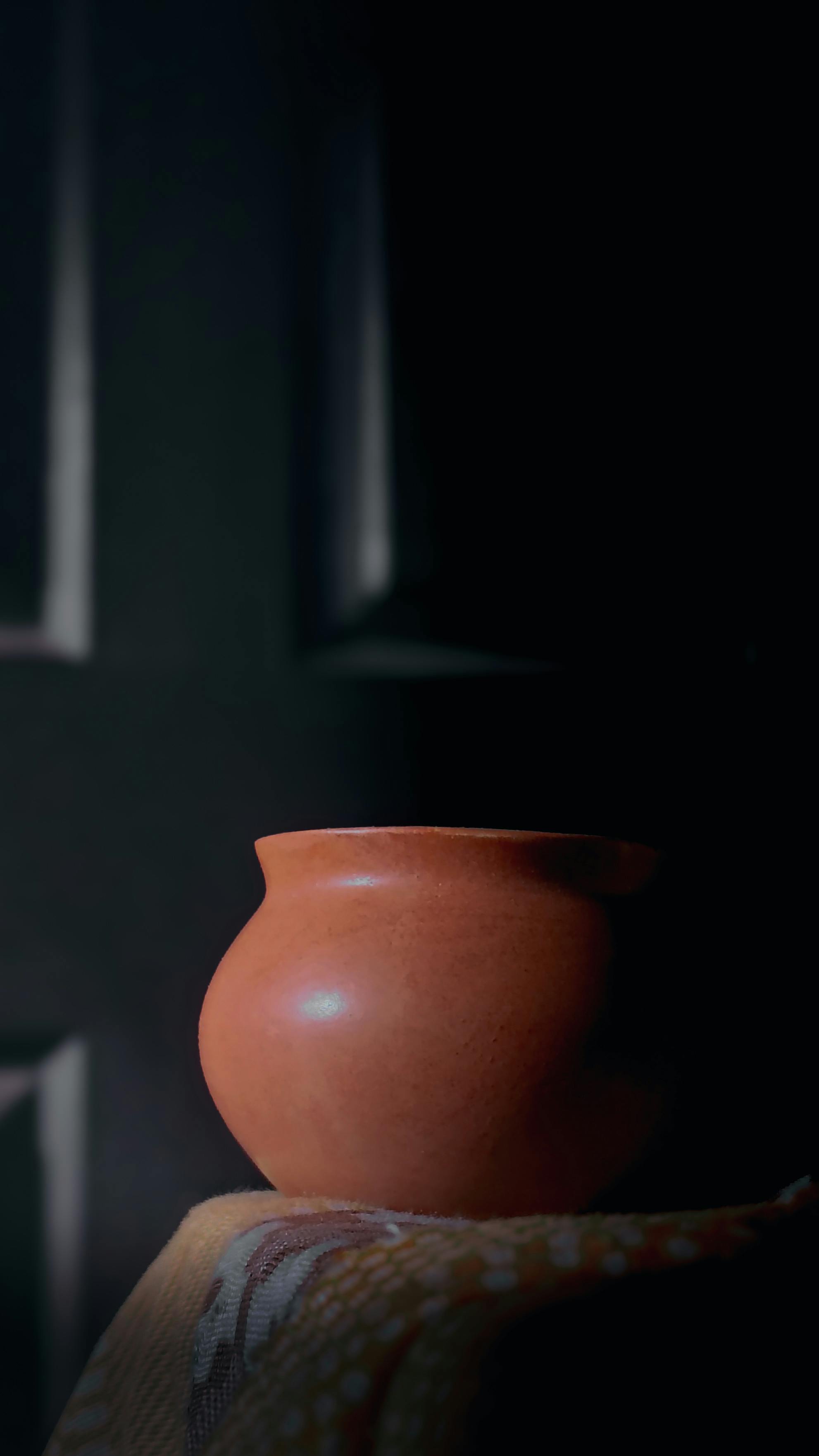 Gratis Un vaso di terracotta rustico è illuminato da una luce soffusa, creando un'atmosfera calda e terrosa. Foto a disposizione