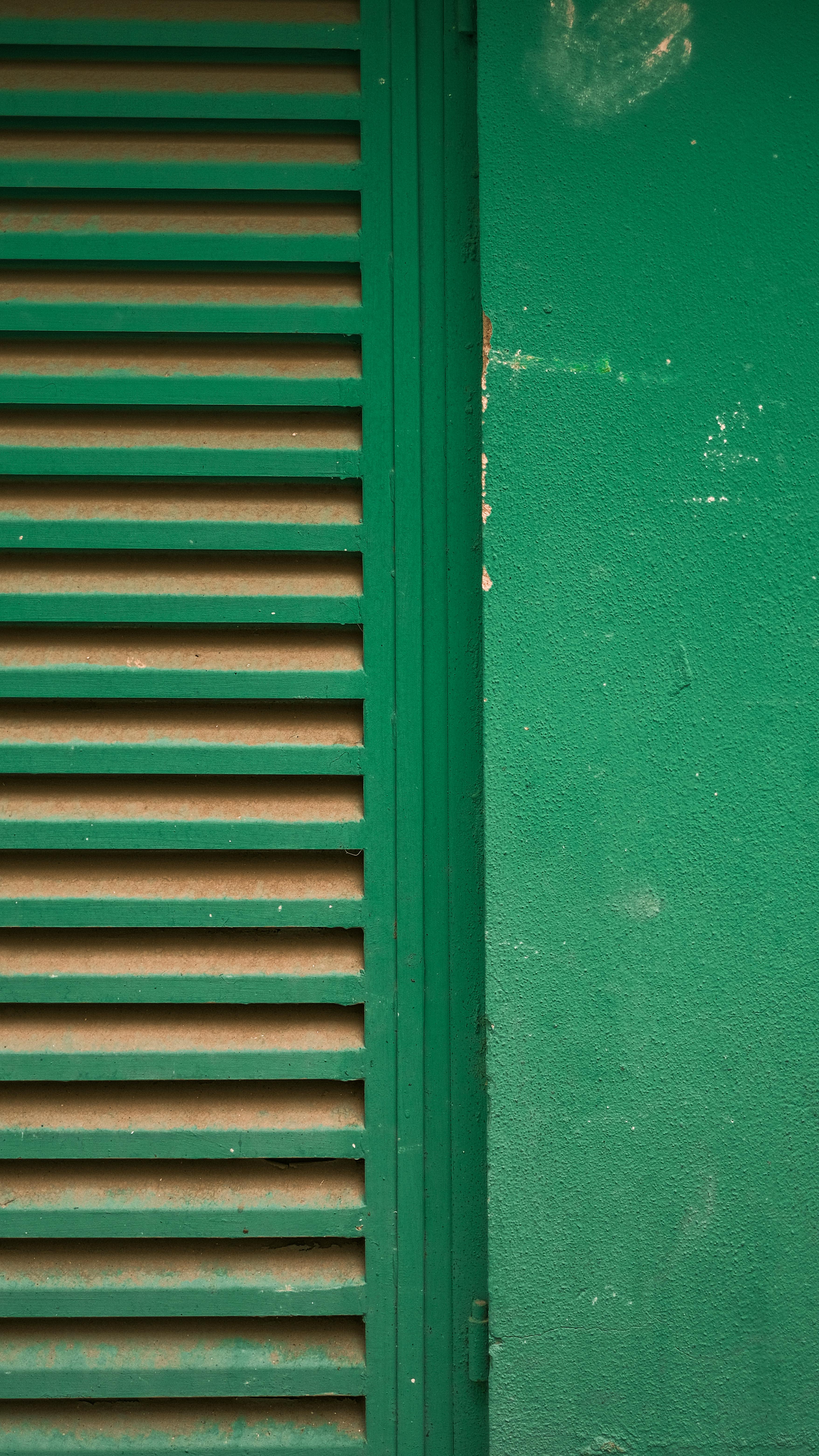 Free Close-up of a green louvered shutter next to a textured wall, ideal for background or design elements. Stock Photo