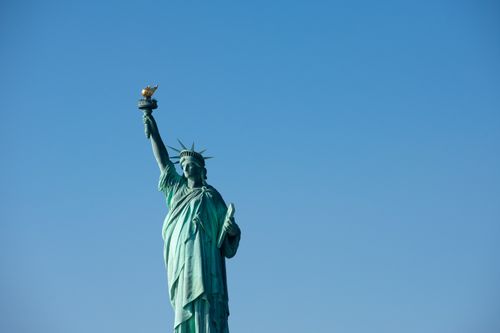Free Iconic Statue of Liberty with torch against a bright blue sky, symbolizing freedom. Stock Photo
