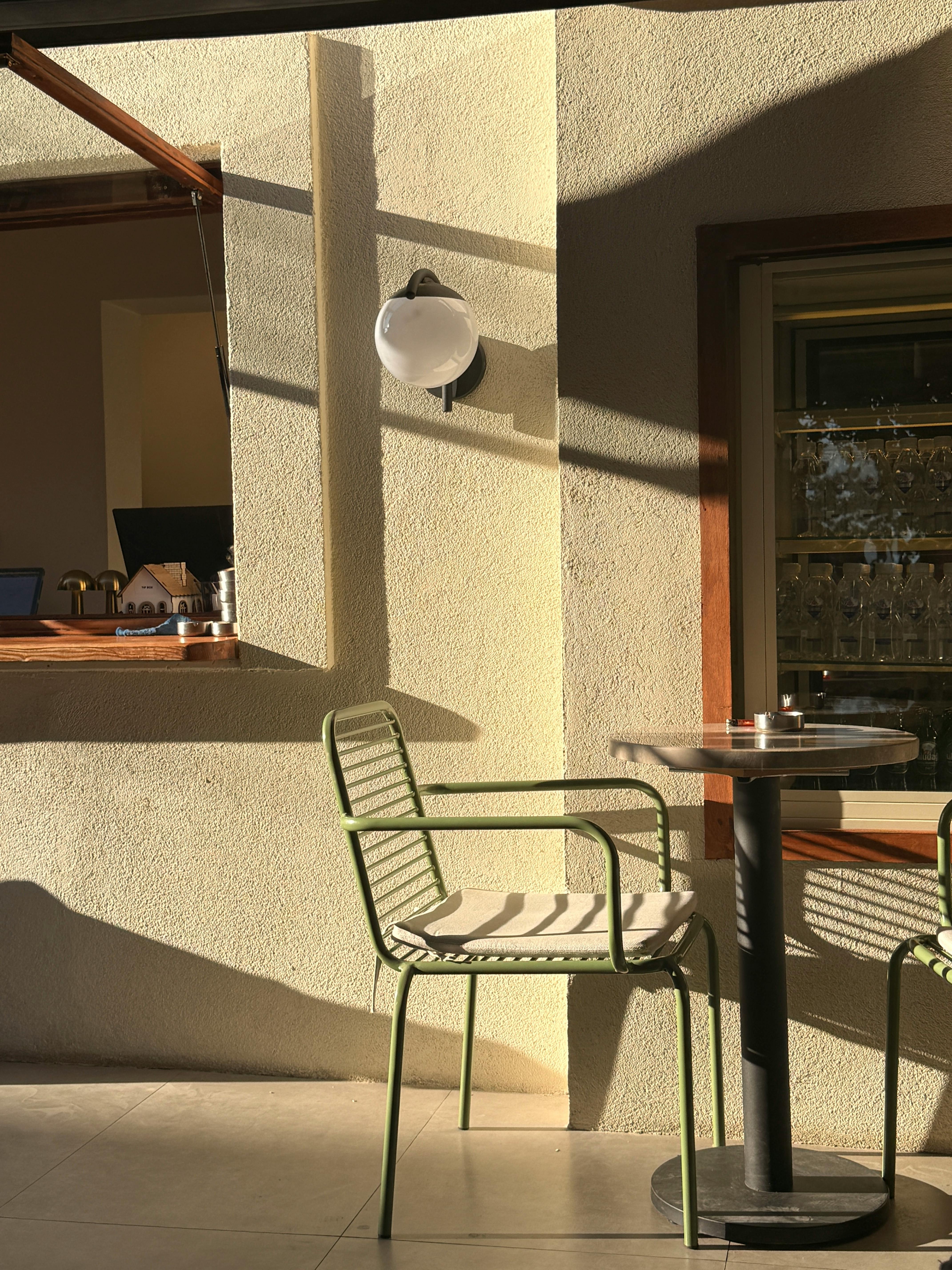 Kostenlos Eine sonnendurchflutete Café-Ecke mit eleganten Stühlen und Tisch, die sanfte Schatten werfen. Stock-Foto