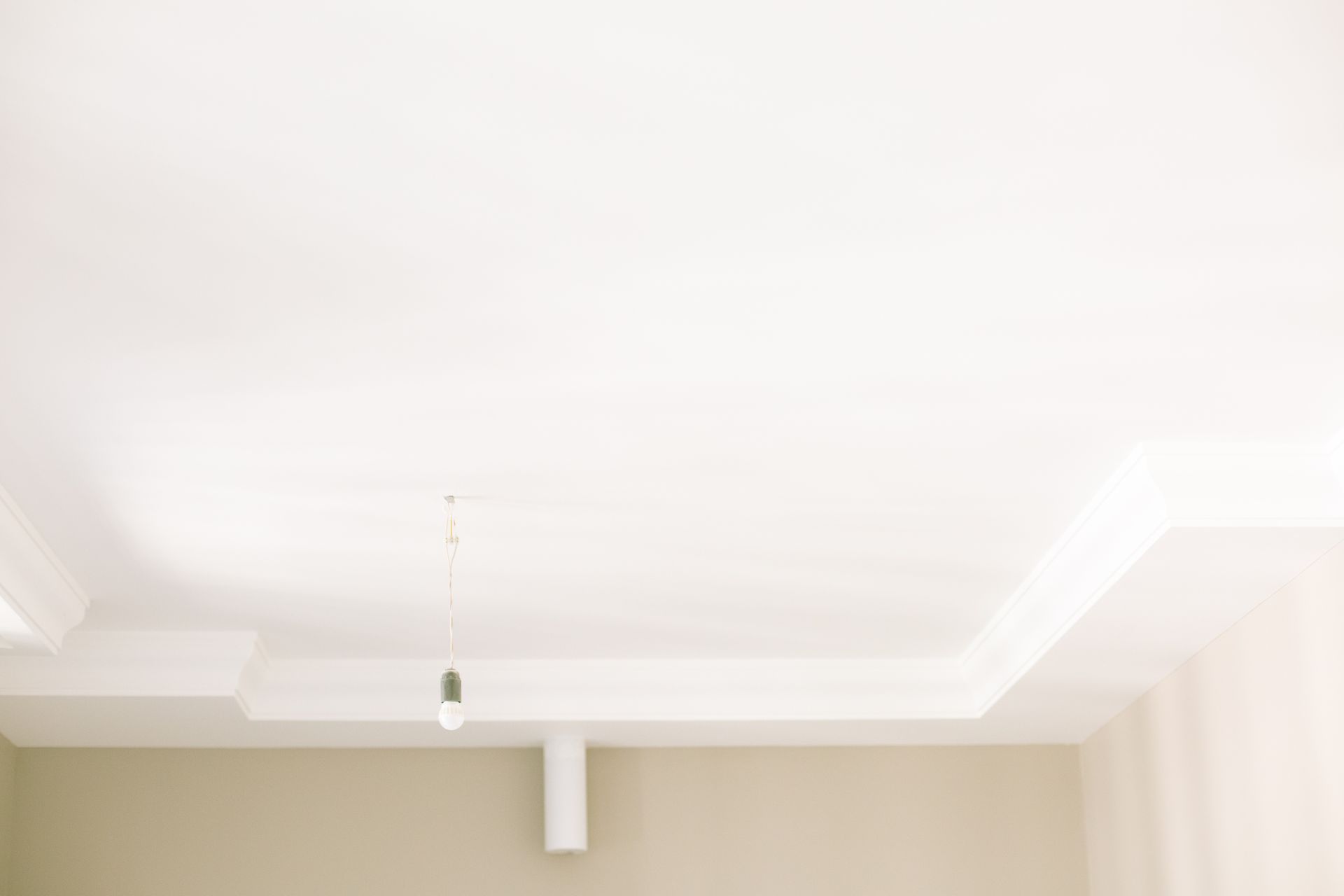 Bright white ceiling with a single hanging light bulb highlighting minimal interior design.