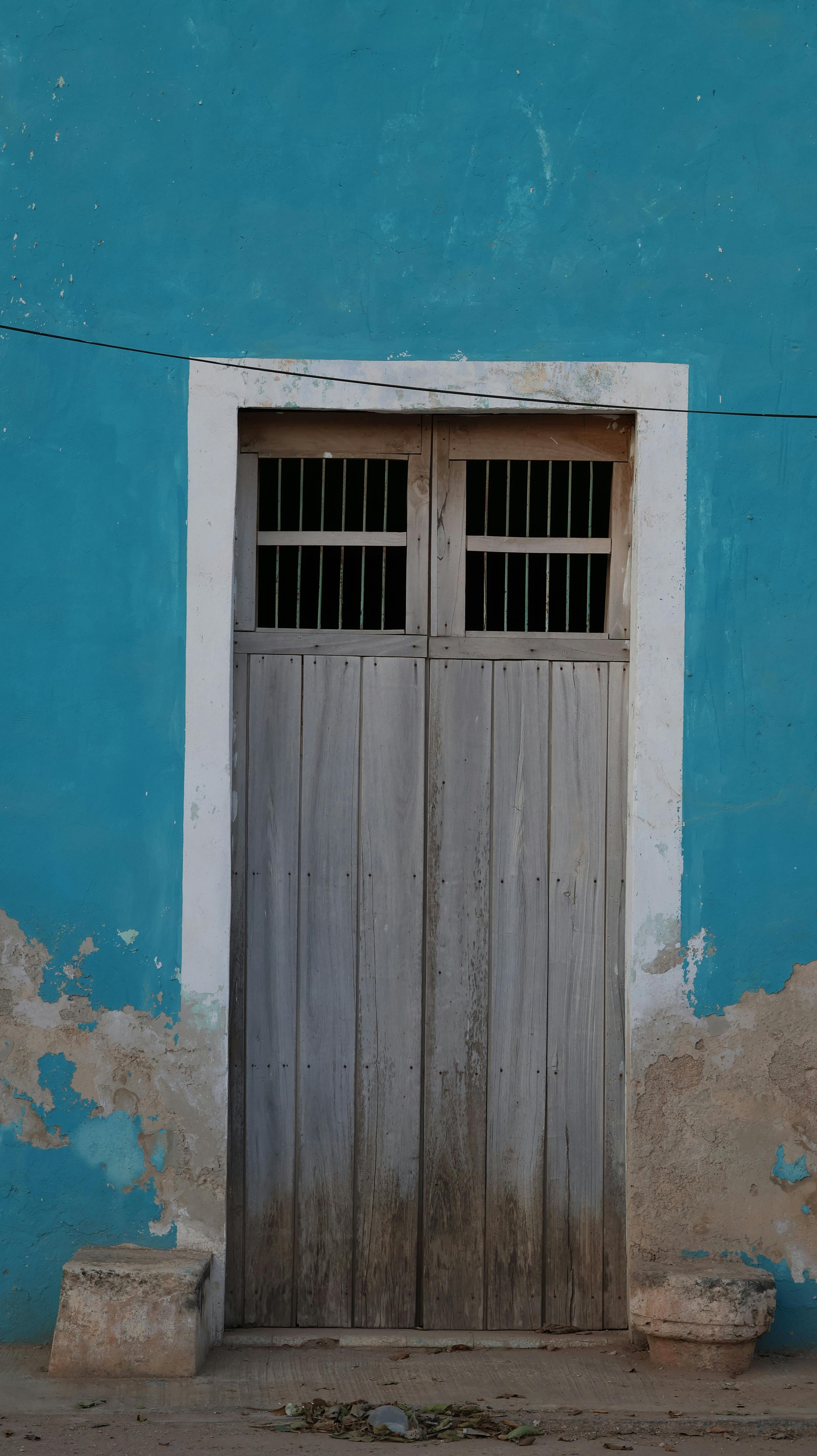 Kostenlos Eine rustikale Holztür im Kolonialstil vor einer leuchtend türkisfarbenen Wand in Yucatán. Stock-Foto