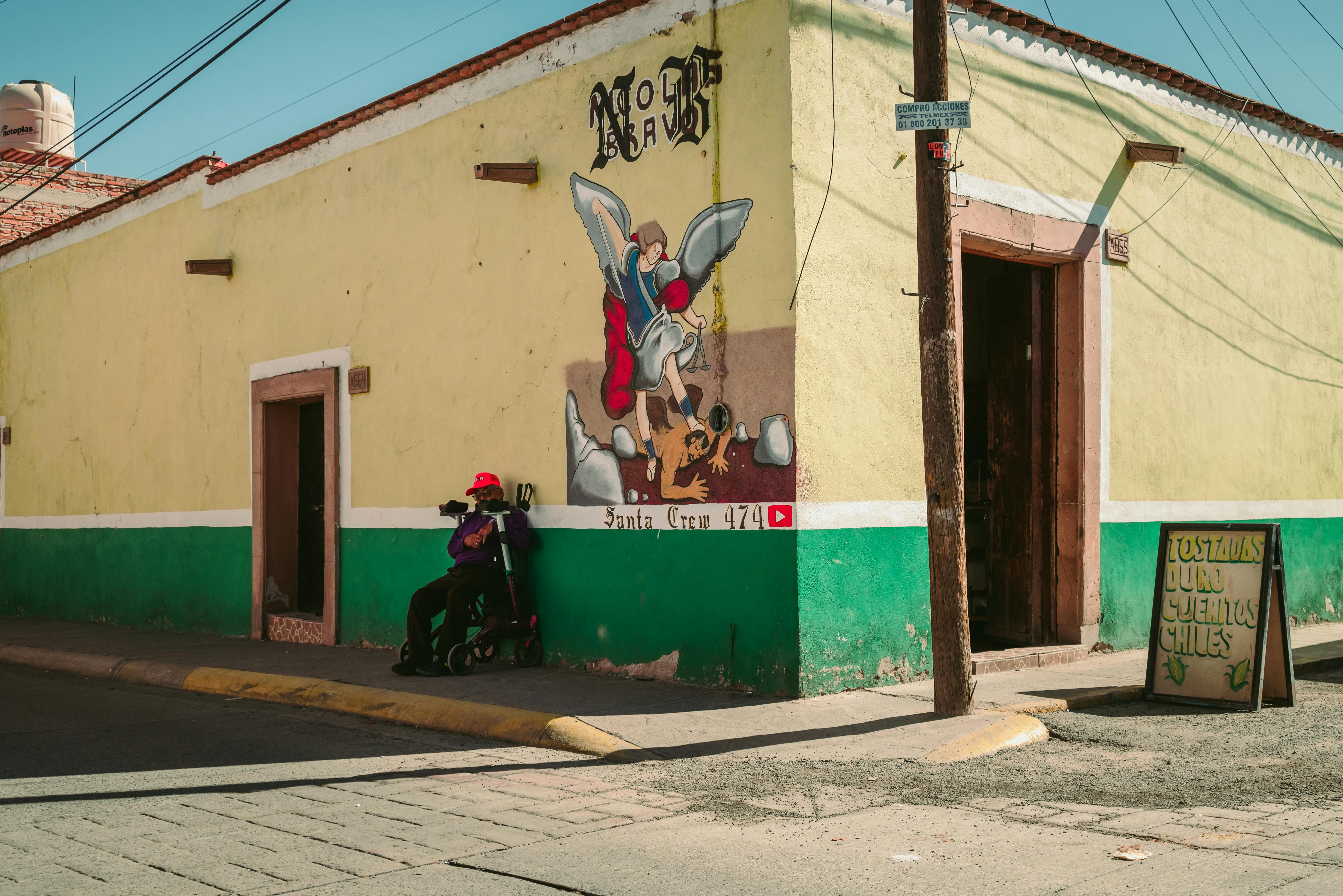 Gratis Una esquina vibrante con un mural, una persona descansando y un cartel que anuncia chiles. Foto de stock