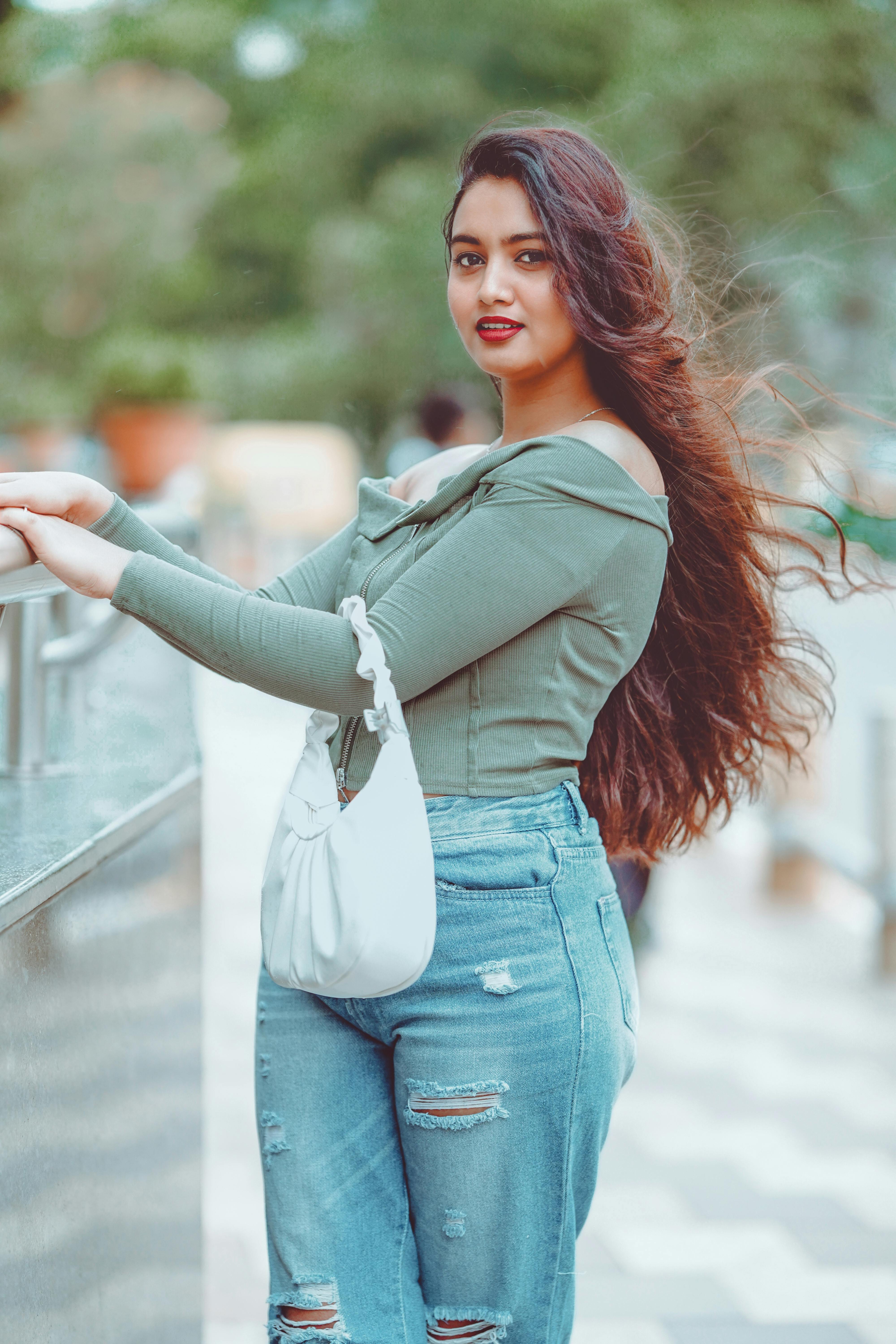 ฟรี หญิงสาวในชุดลำลองกางเกงยีนส์และเสื้อ ยืนโพสท่าอย่างมั่นใจกลางแจ้ง ผมยาวสลวย คลังภาพถ่าย