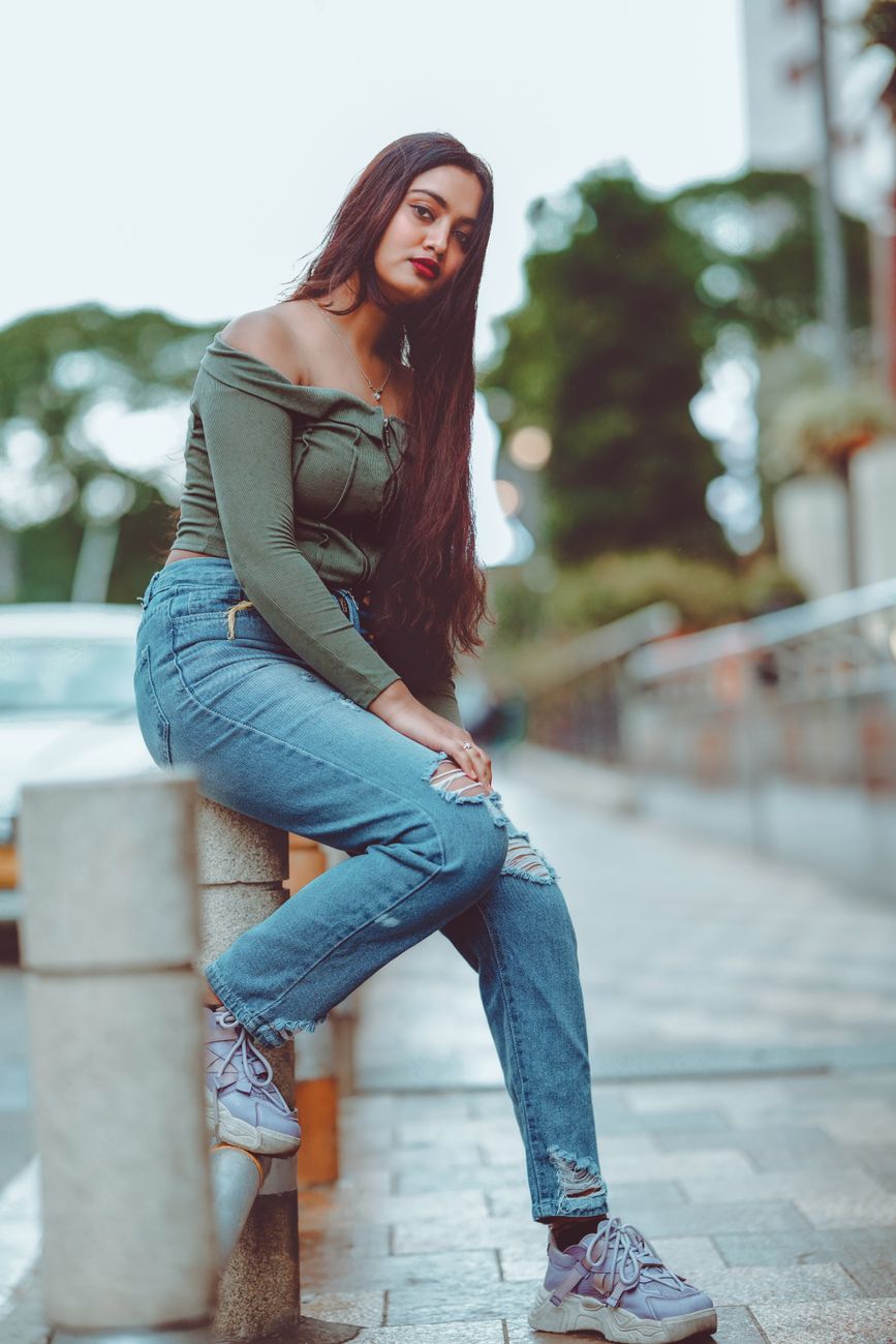 Confident woman in casual fashion poses on a city street bench, exuding modern style and attitude.