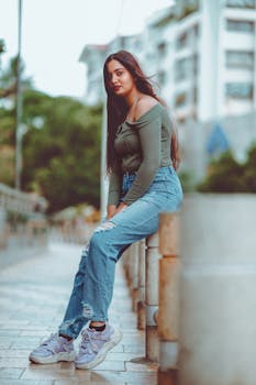 Fashionable young woman seated on a city street, showcasing casual style with denim jeans.