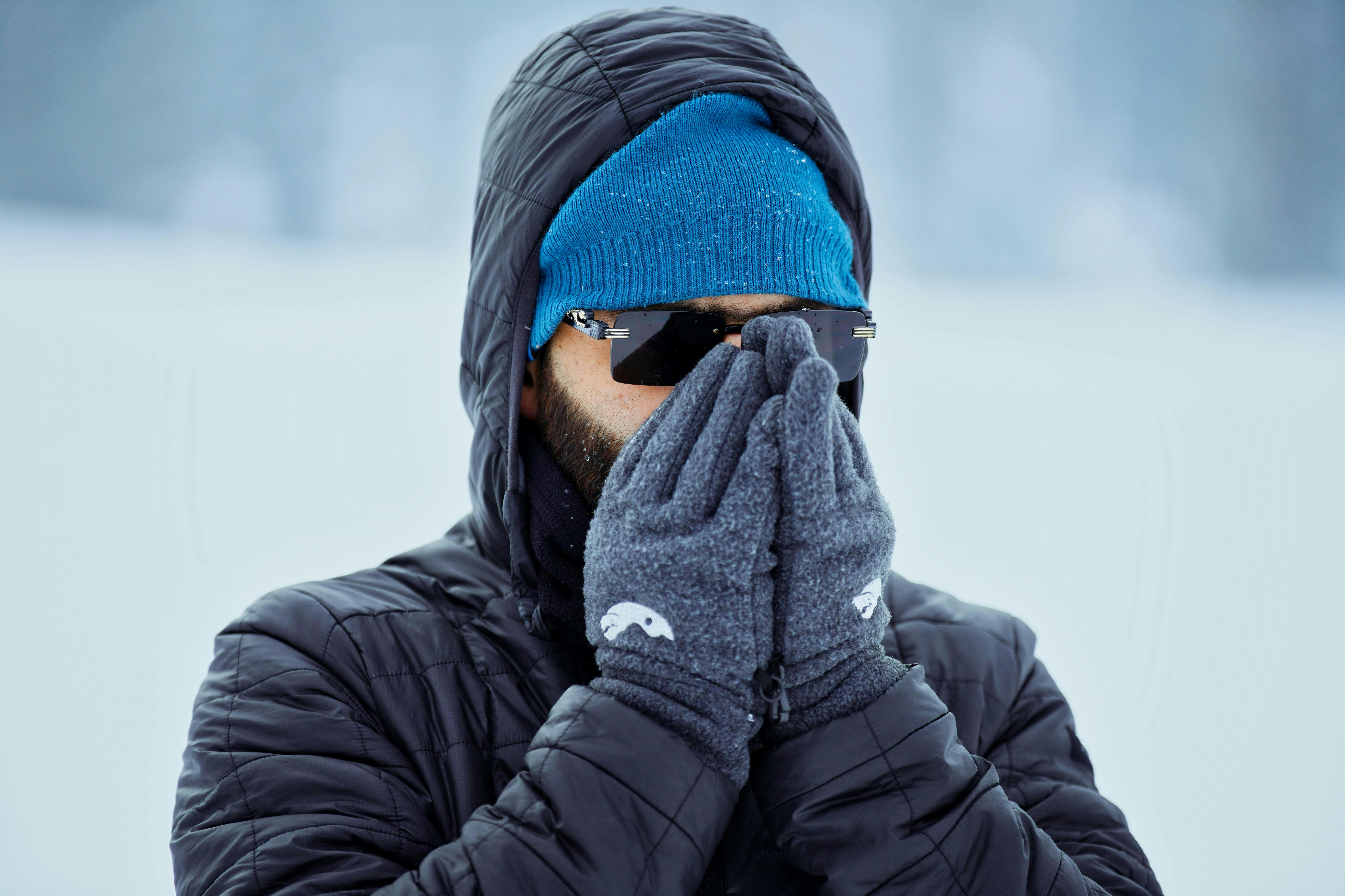Adult male bundled in winter gear with gloves and sunglasses outdoors in cold weather.
