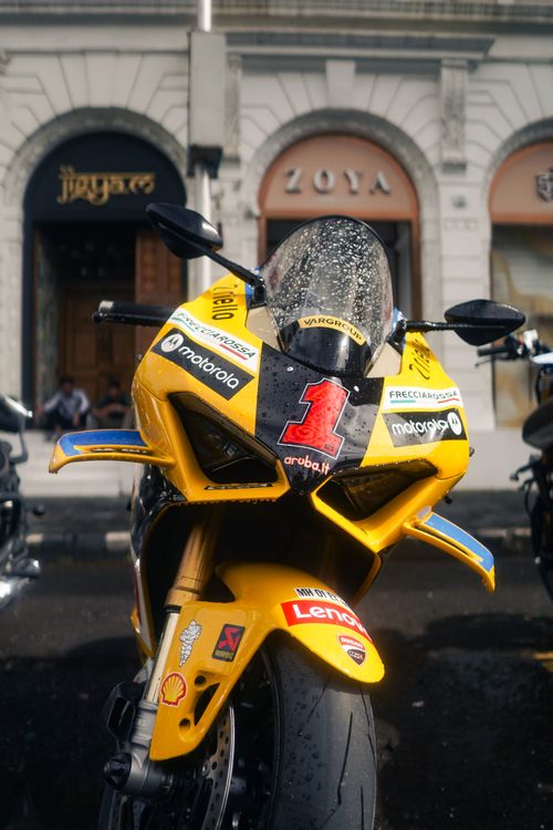 Free Front view of a yellow racing motorcycle with decals, parked in a city street. Stock Photo